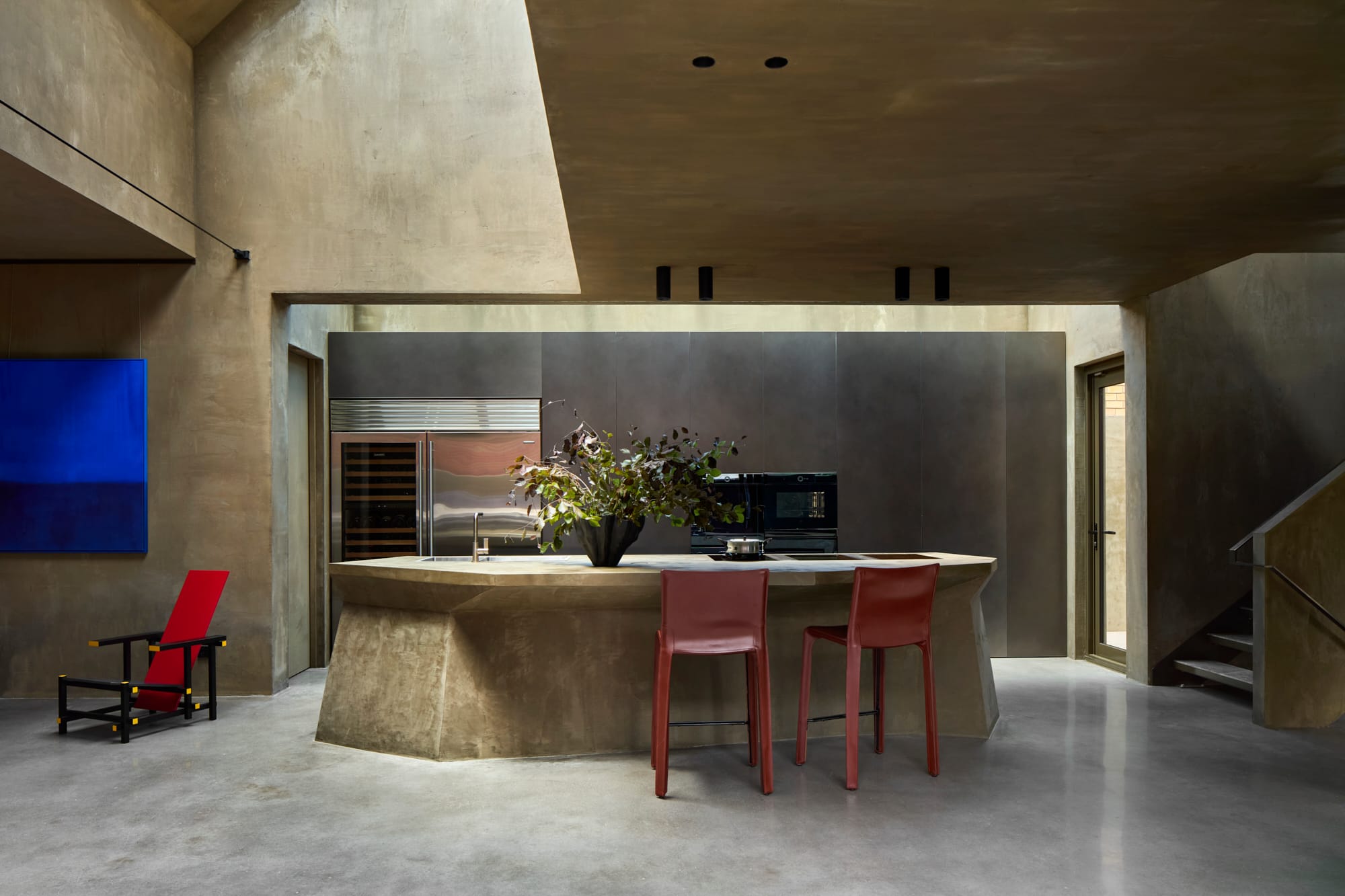 Proclamation House by State of Kin. View to customised hempcrete kitchen island featuring sharp edges, skylight and brick colored bar stools.