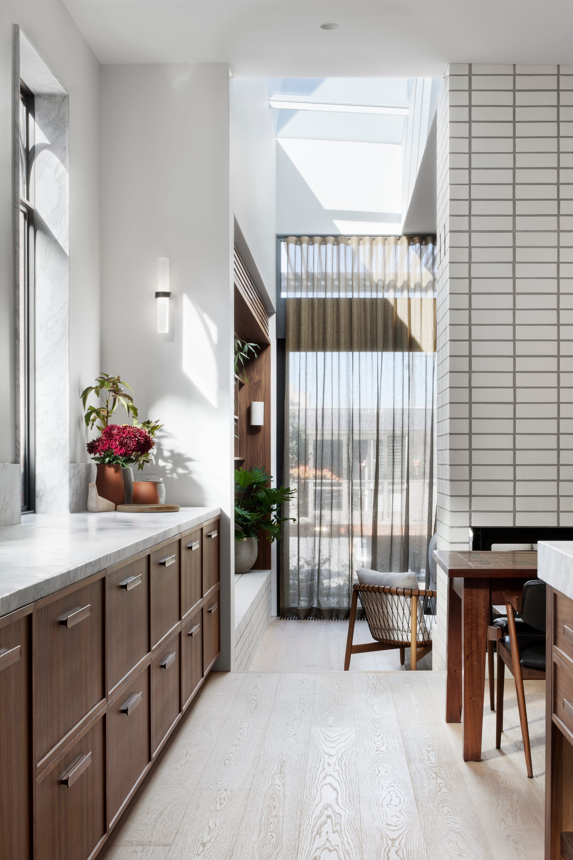 South Terrace Residence by Chan Architecture. Kitchen featuring walnut wood and white marble worktop with view to living space.