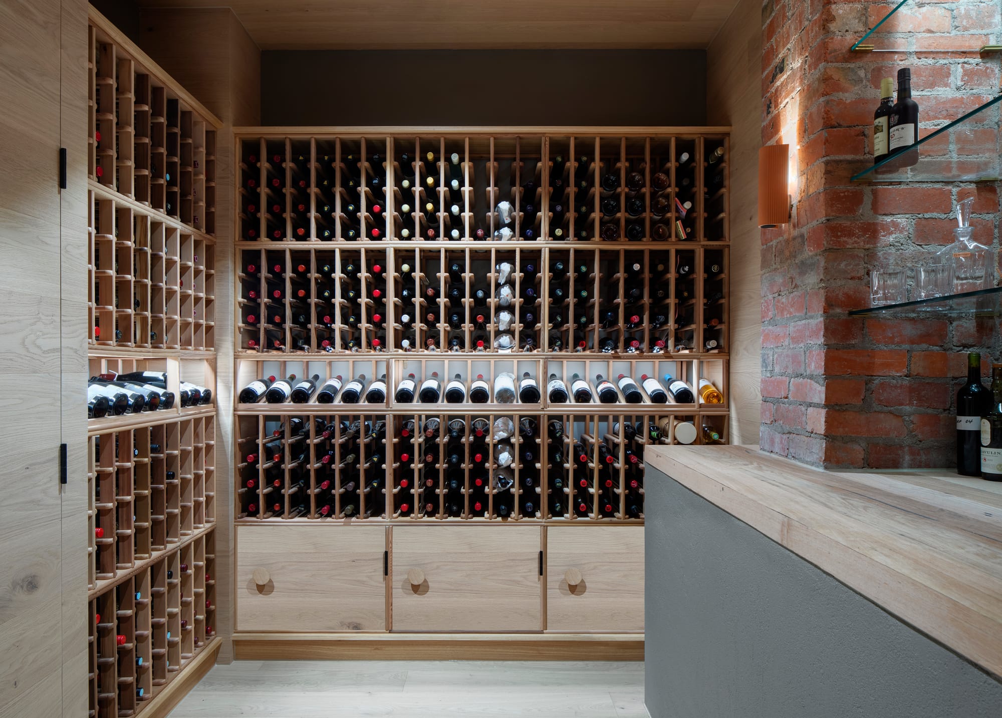 South Terrace Residence by Chan Architecture. Wine cellar featuring oak fitted shelving and red brick wall.