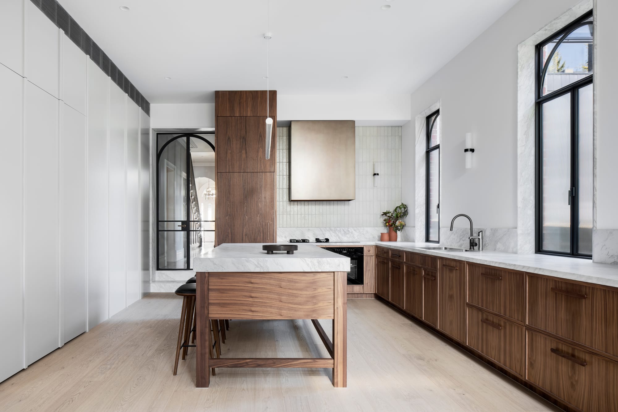 South Terrace Residence by Chan Architecture. Kitchen featuring walnut wood cabinets, kitchen island and white varnished fitted floor to ceiling cabinet.