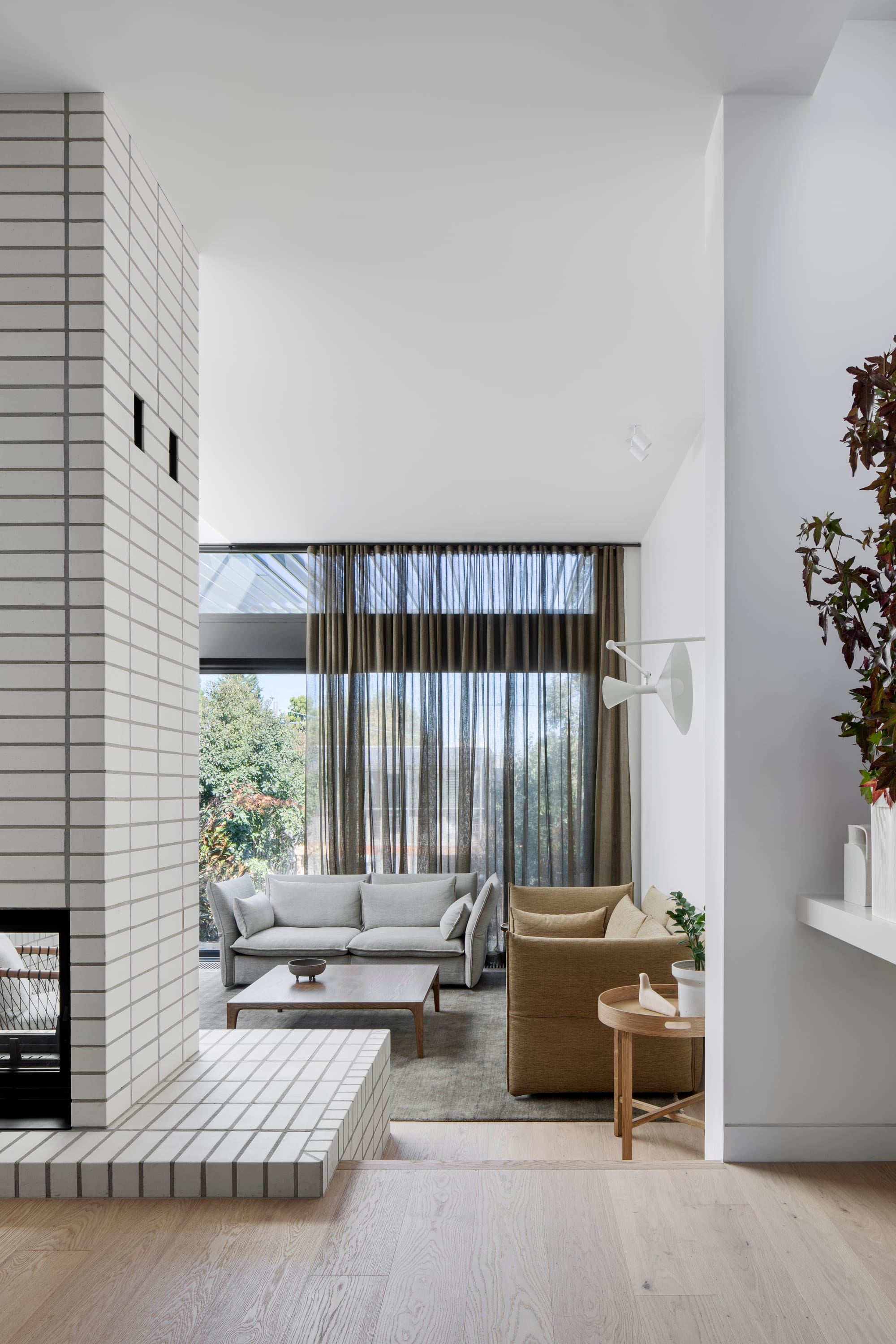 South Terrace Residence by Chan Architecture. View to living room featuring white brick wall, integrated chimney and floor to ceiling windows.