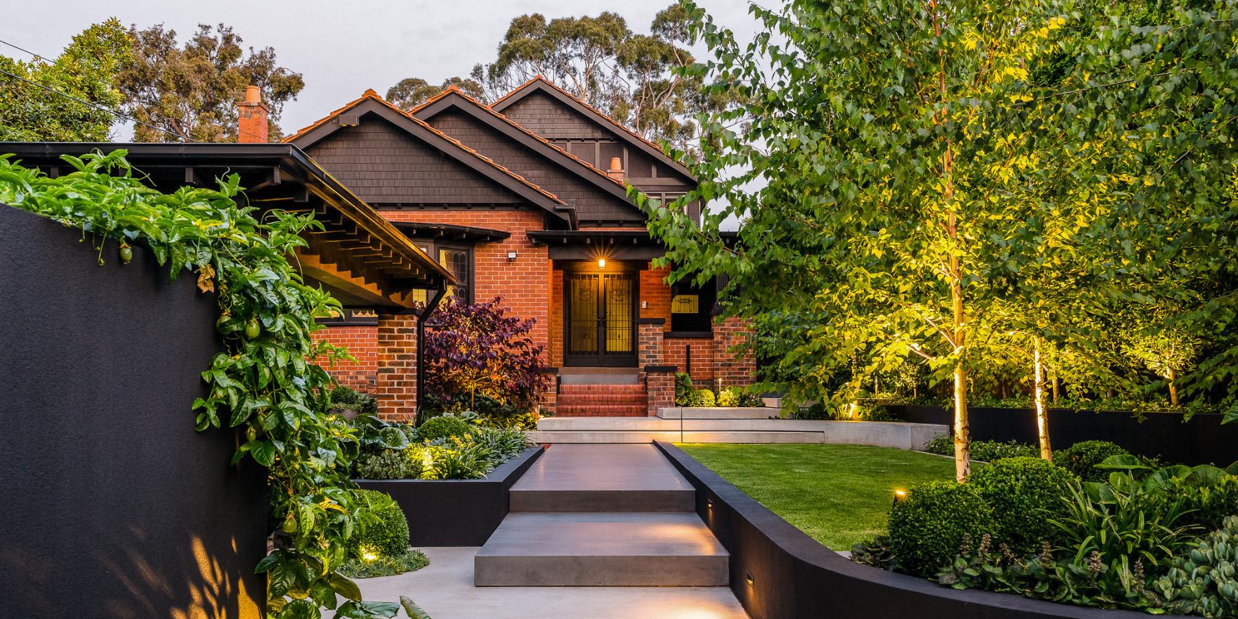 Outside view on red brick house featuring garden and layered concrete hardscaping stairway. 