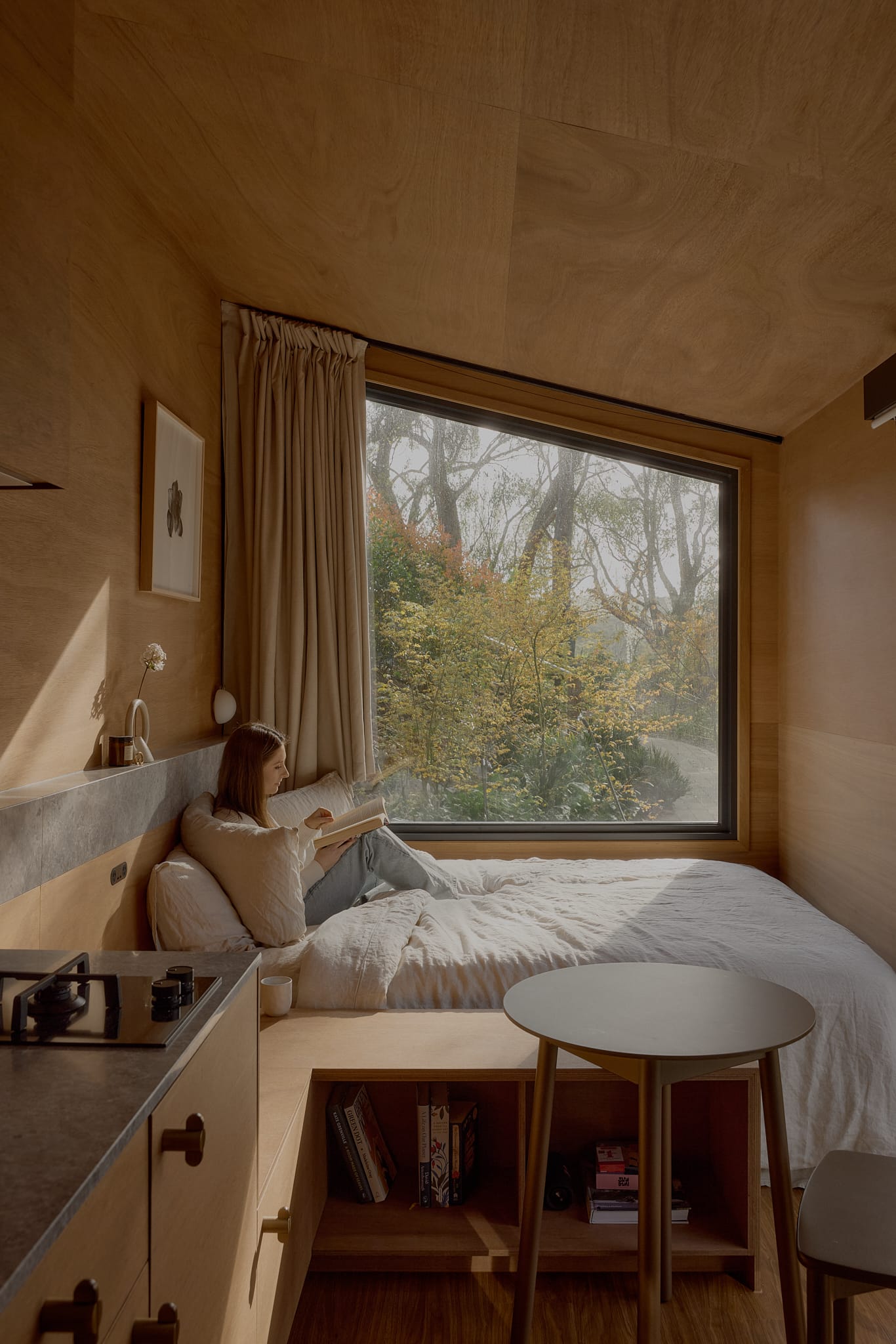 Brook James by Base Cabin. Wooden, minimalistic tiny house interior with view to bedroom featuring large window with view to nature.