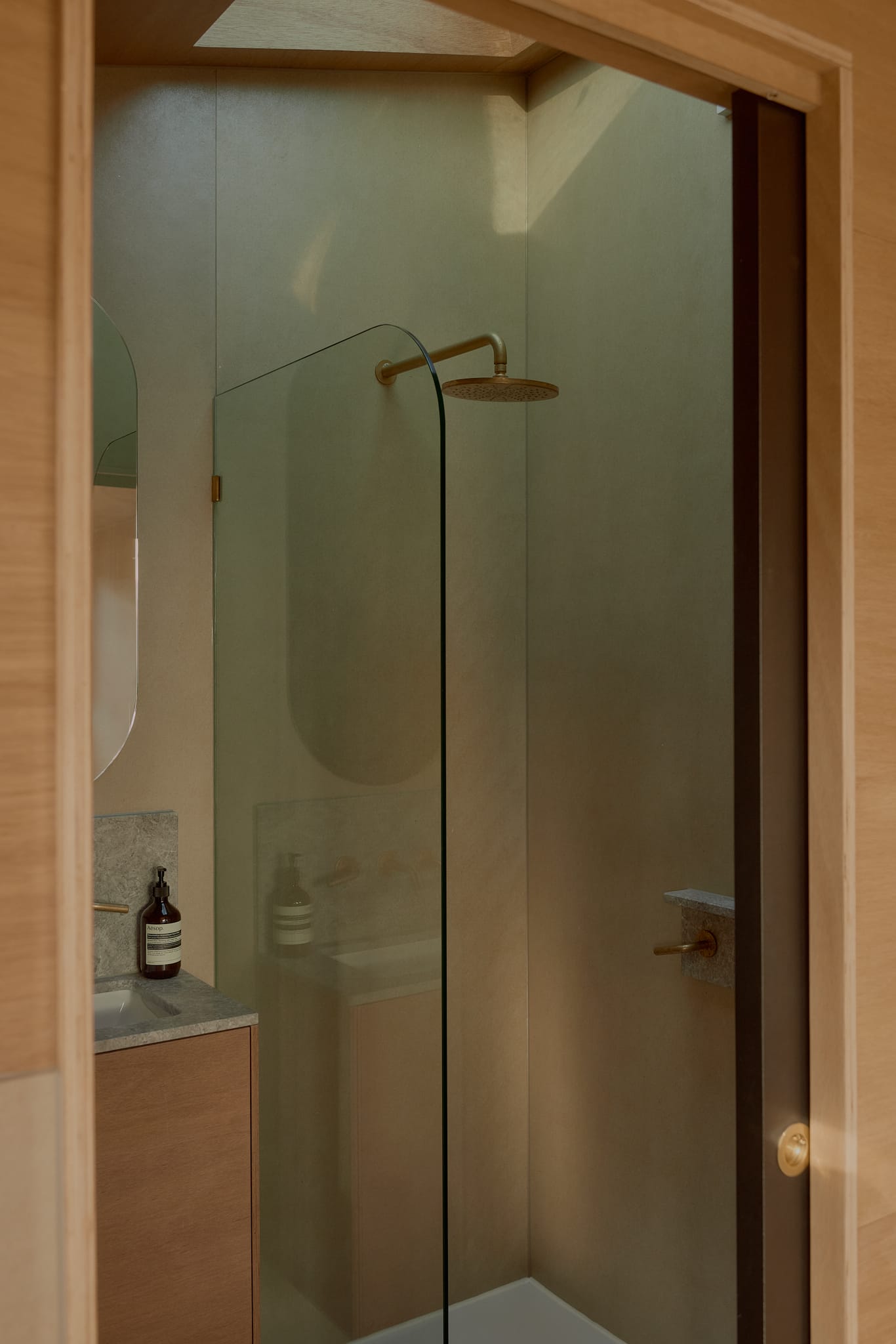 Brook James by Base Cabin. Tiny house bathroom featuring plywood interior, oval mirror and shower skylight.