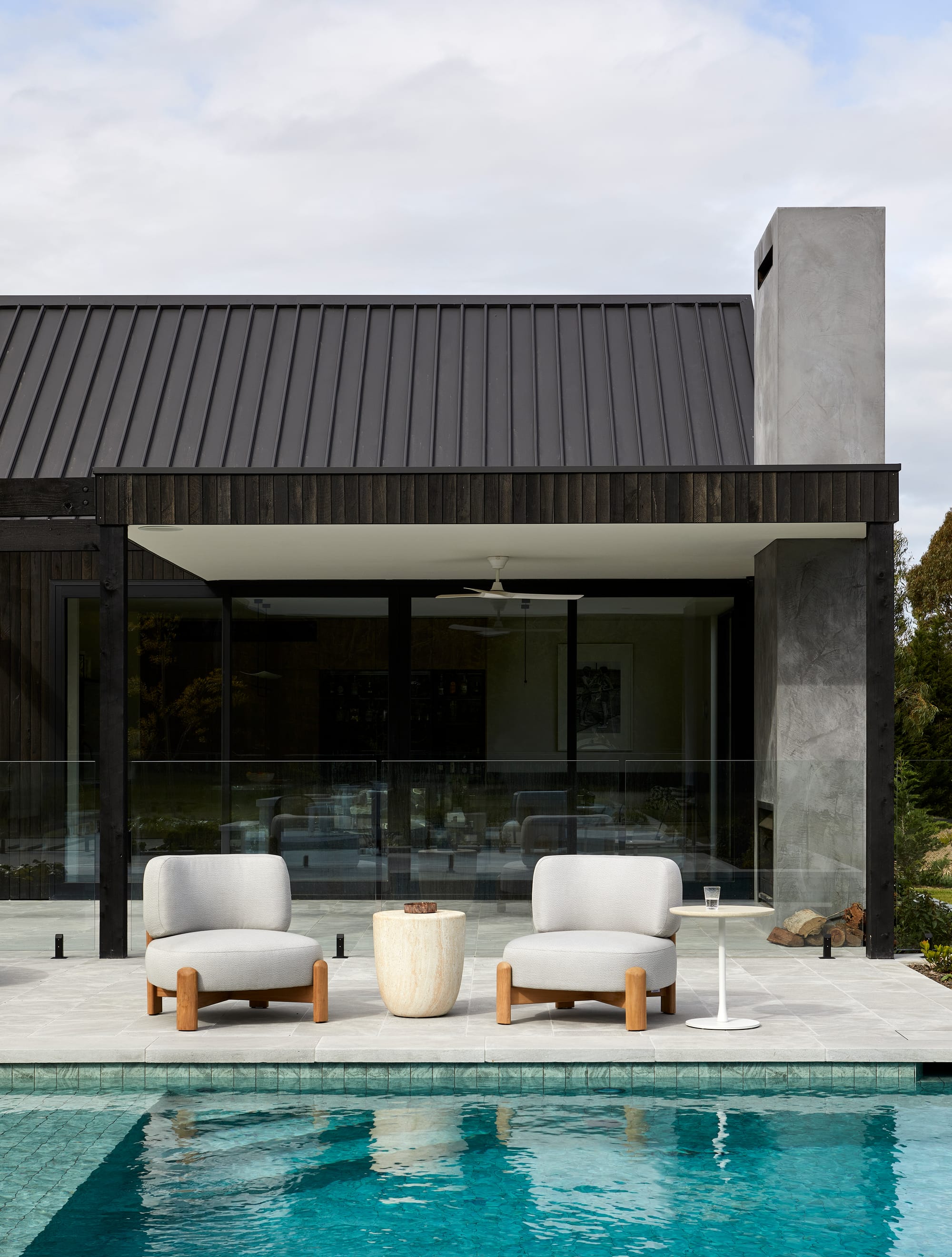 Dawn Occasional Chairs by GlobeWest. White lounge chairs featuring tweak wood base and beige marble table at pool in front of modern building. 