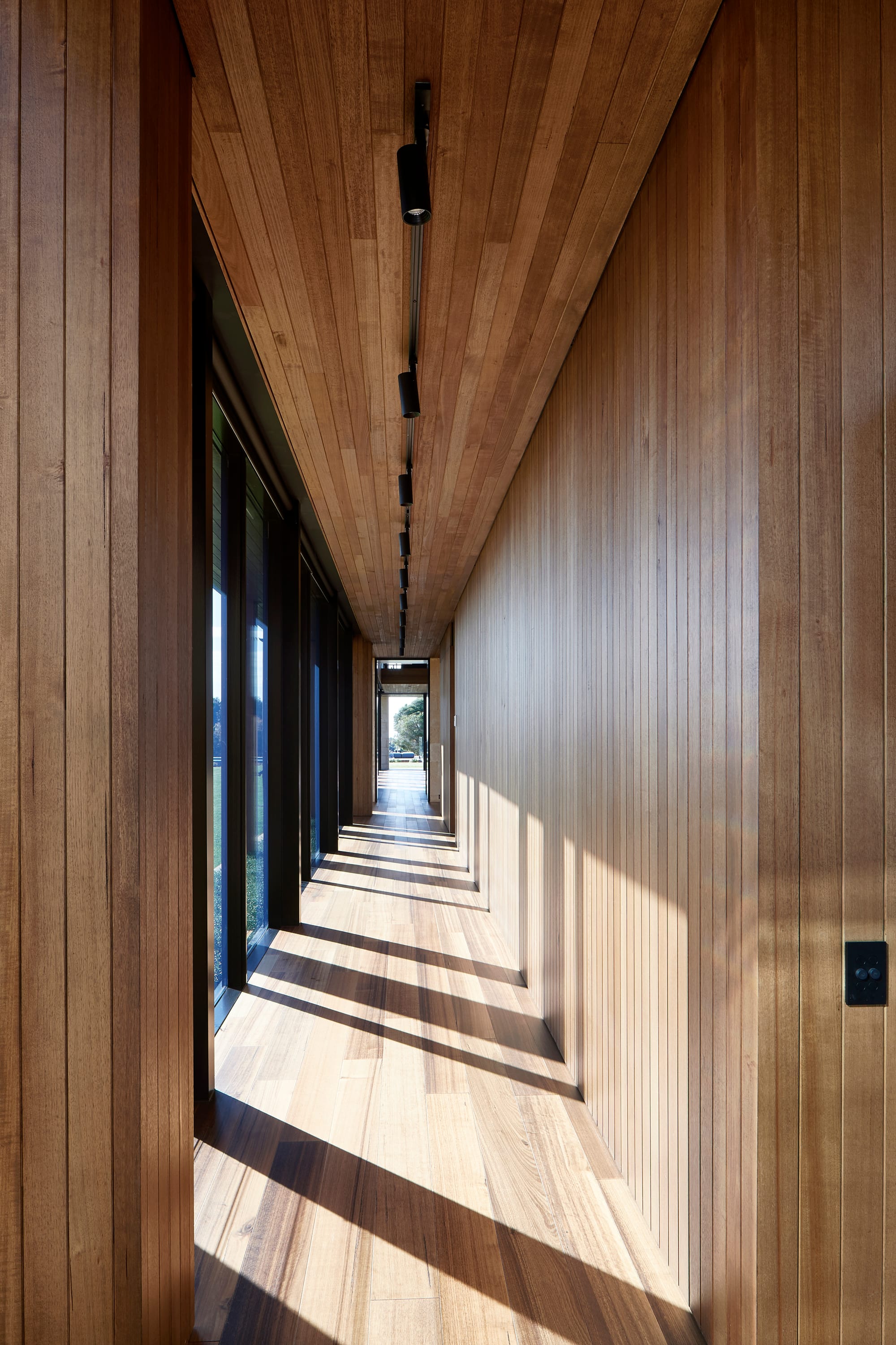 Flinders Residence by Abe McCarthy. Modern residence hallway featuring floor to ceiling windows, Tasmanian oak wood panels and ceiling spotlights.