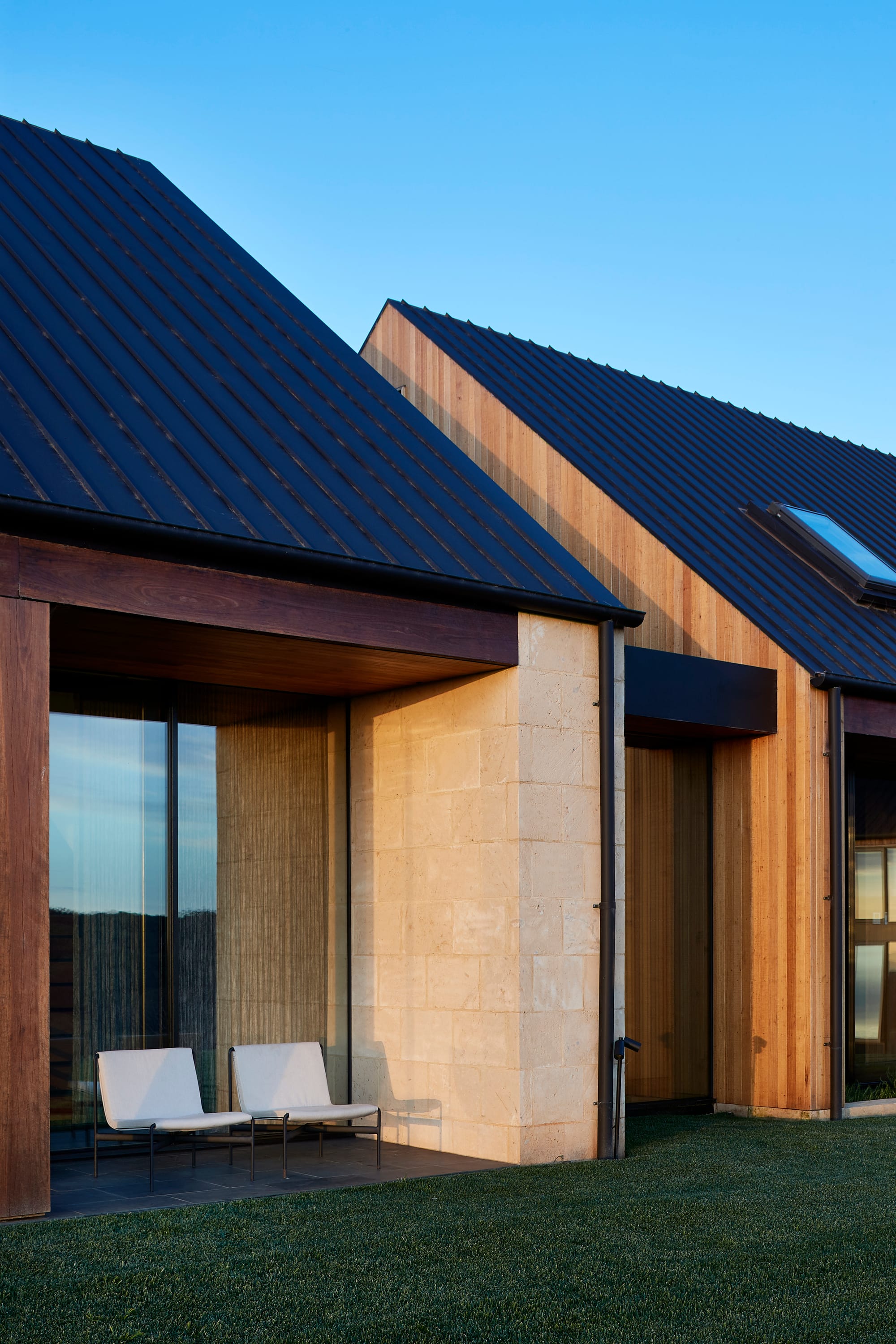 Flinders Residence by Abe McCarthy. Contemporary residence view featuring pitched roof beige sandstone and wood panel facade and floor to ceiling windows.