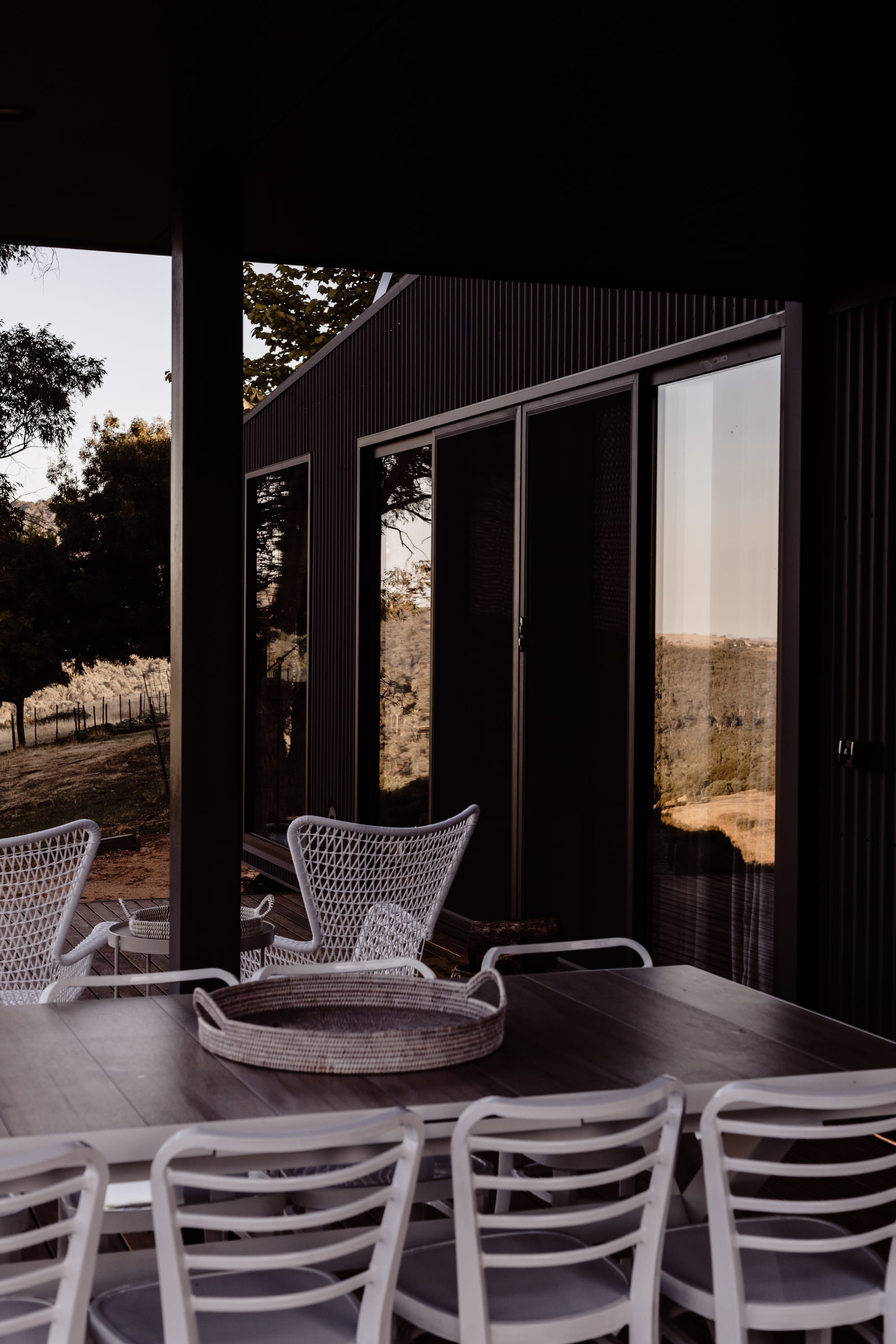 Roam Escape by Roam Merrijing. Luxury accommodation featuring corrugated black facade and outdoor dining area featuring white chairs.