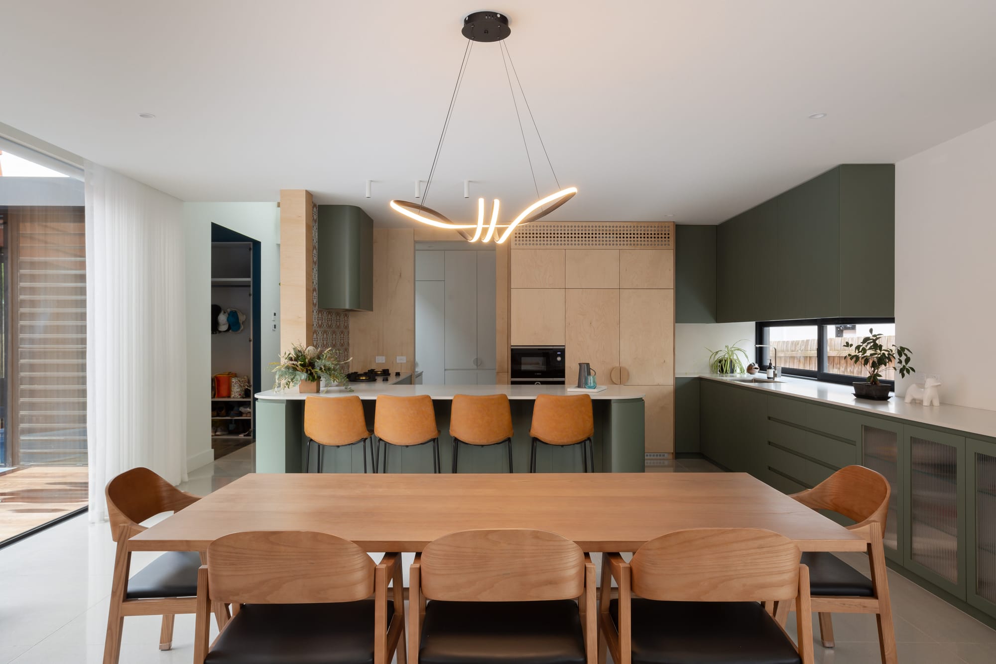 Mahogany House by R Architecture. Modern kitchen area featuring island and dining table opening up to courtyard.