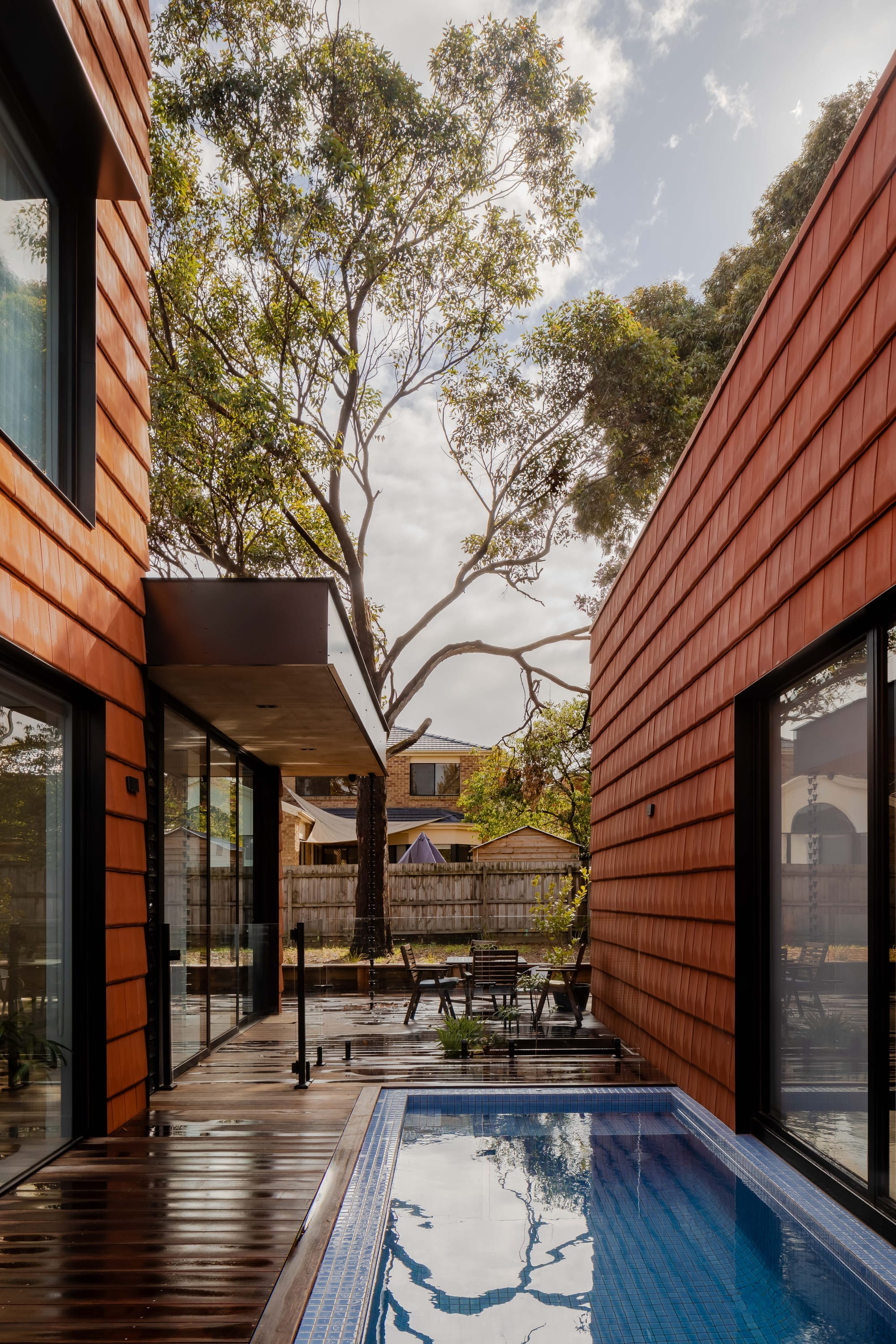 Mahogany House by R Architecture. House units featuring terracotta shingle facade framing patio with outside dining and pool.