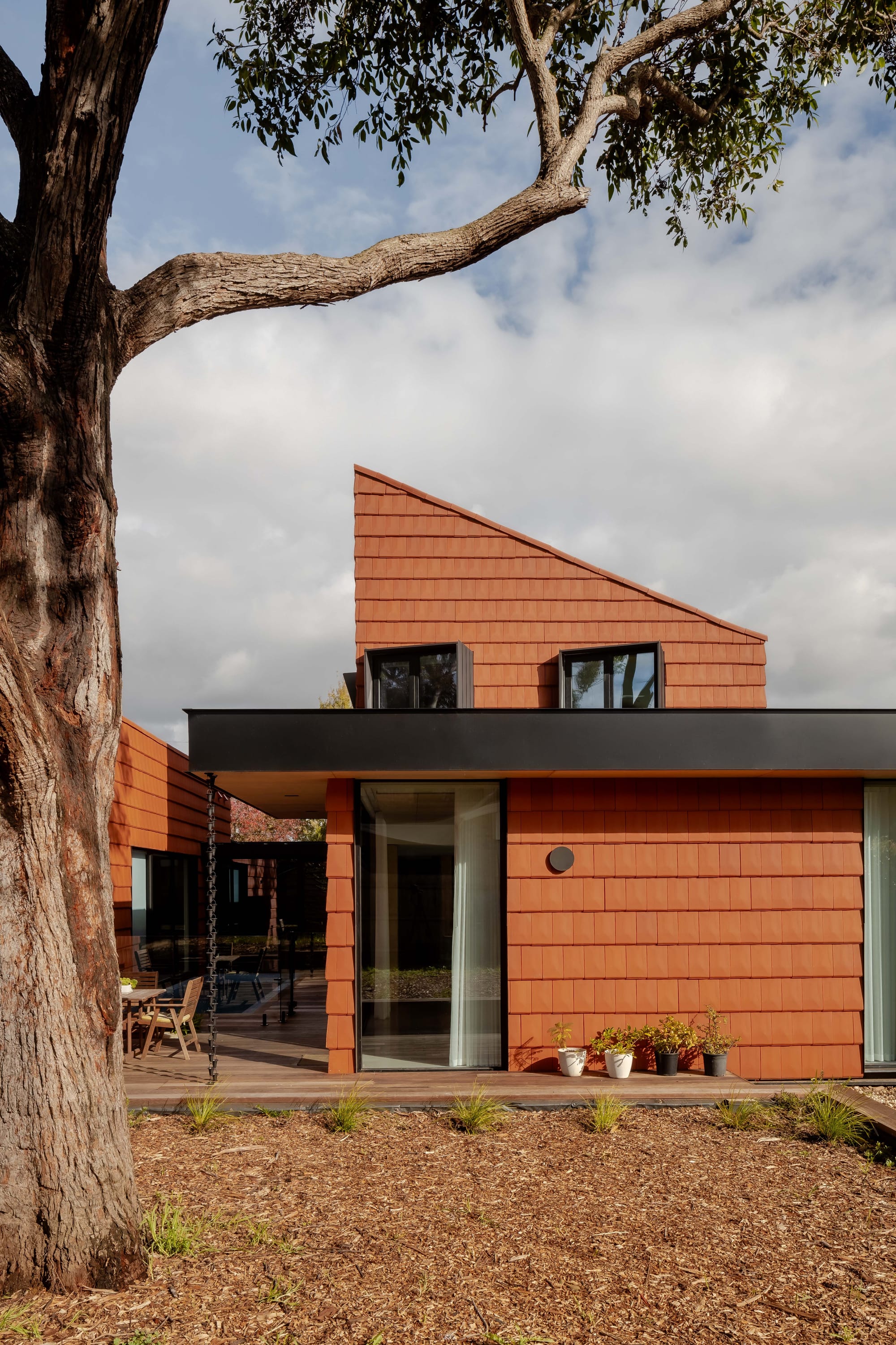 Mahogany House by R Architecture. House units featuring terracotta shingle facade facing patio with outside dining and pool.