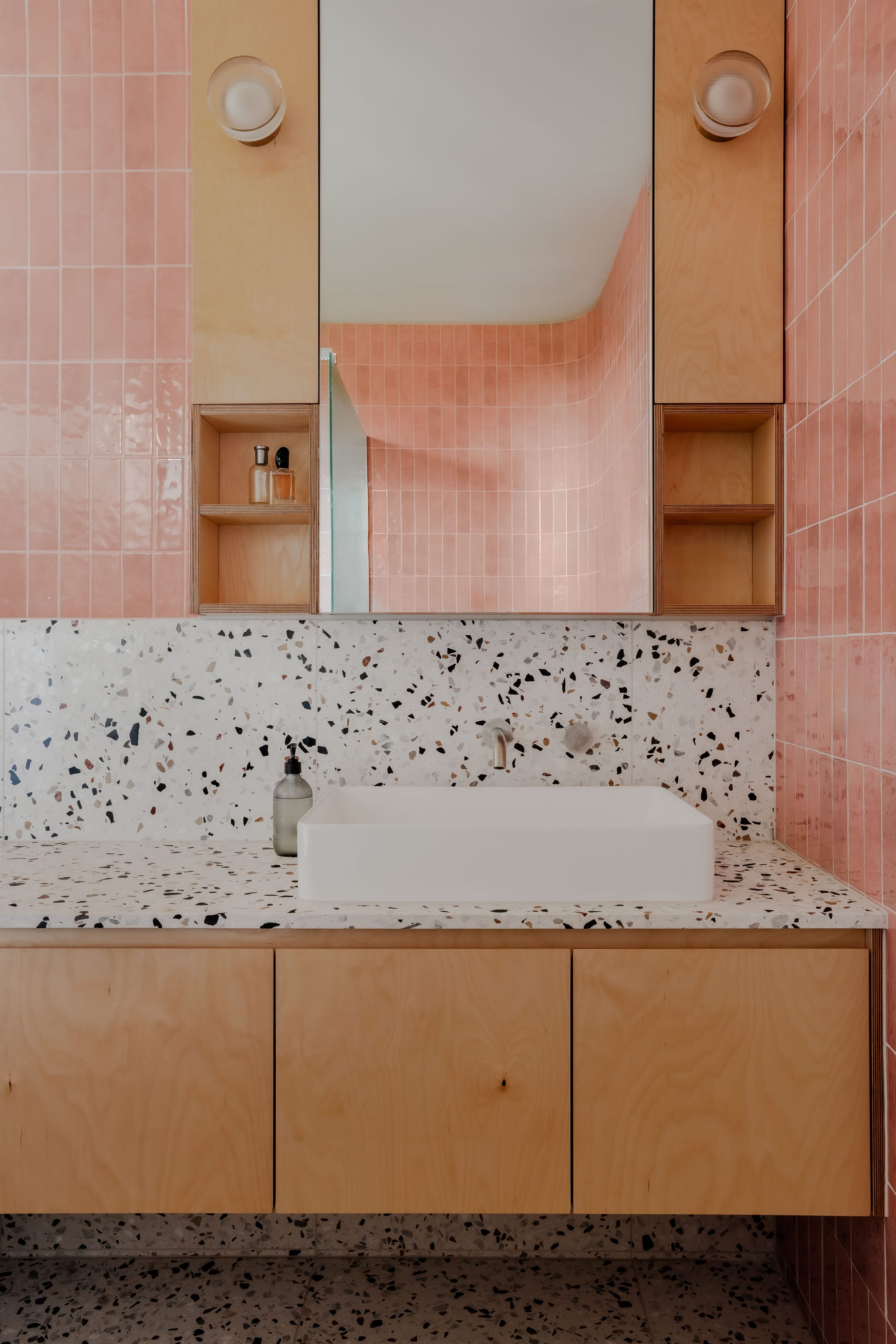 Mahogany House by R Architecture. Modern bathroom featuring pink ceramic tiles, plywood cabinet with white terrazzo surface.