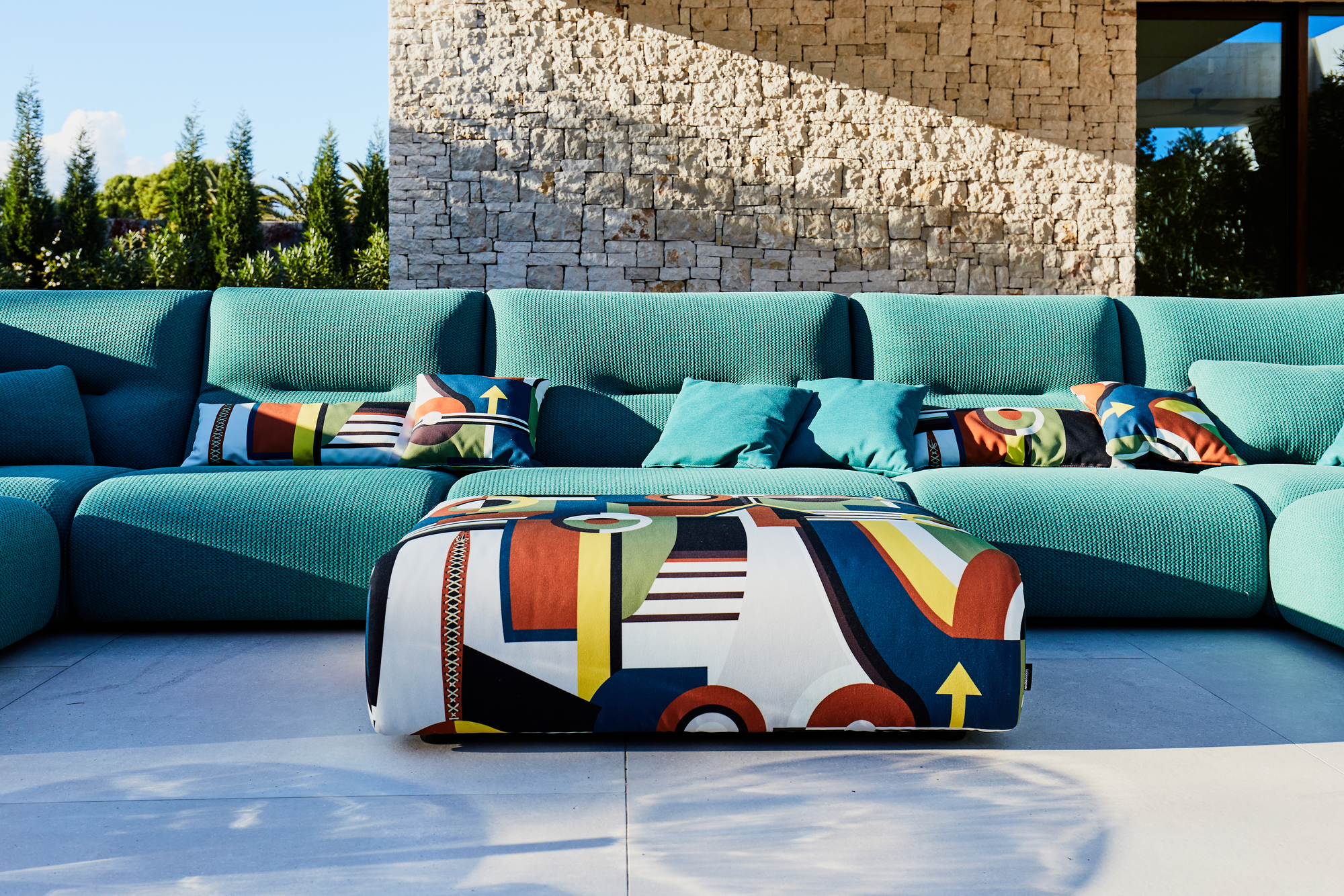 Outdoor Collection by Roche Bobois. Turquoise outdoor sofa next to modern house and pool.