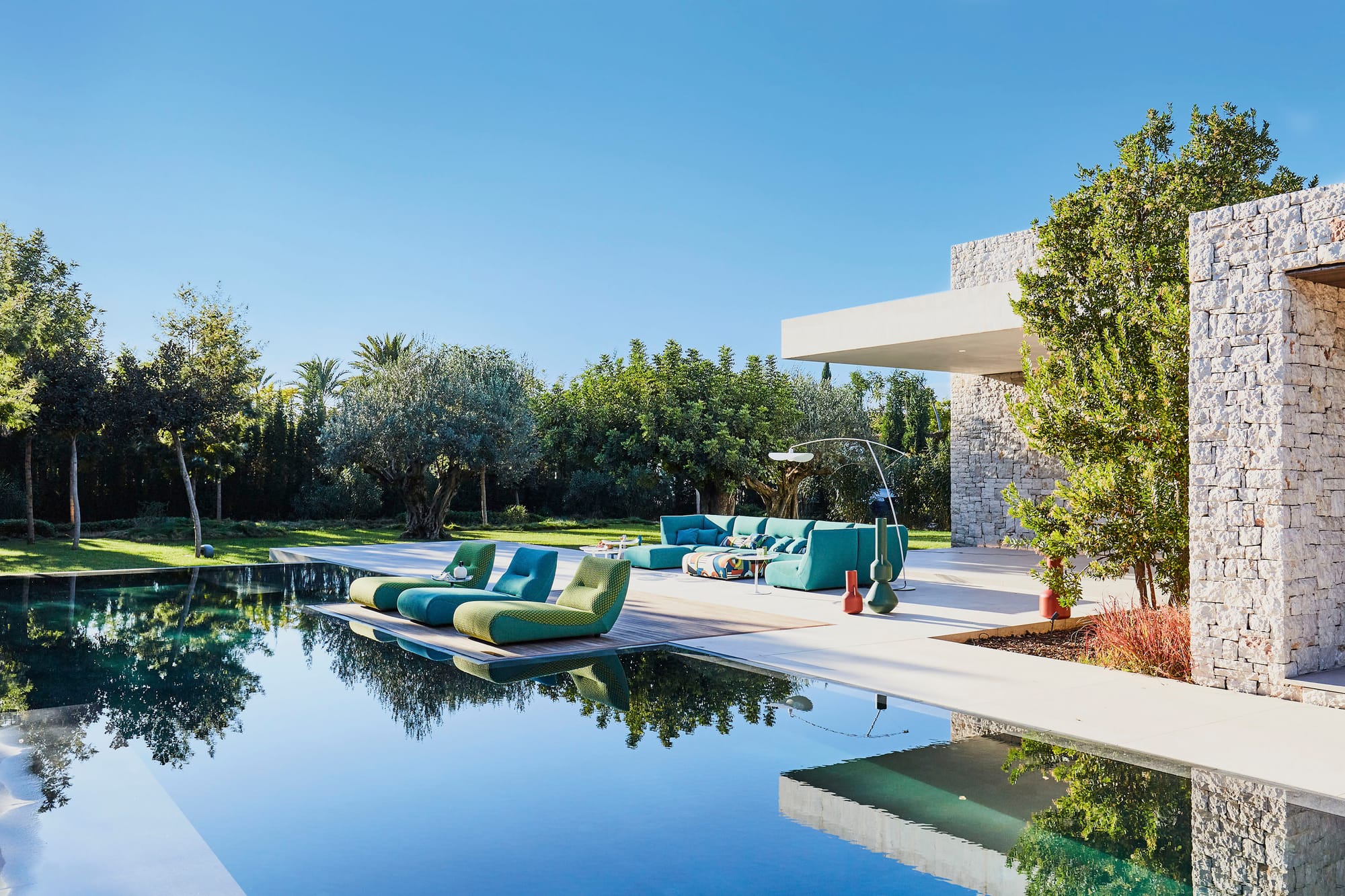 Outdoor Collection by Roche Bobois. Turquoise outdoor sofa and foam sun beds next to modern house and pool.