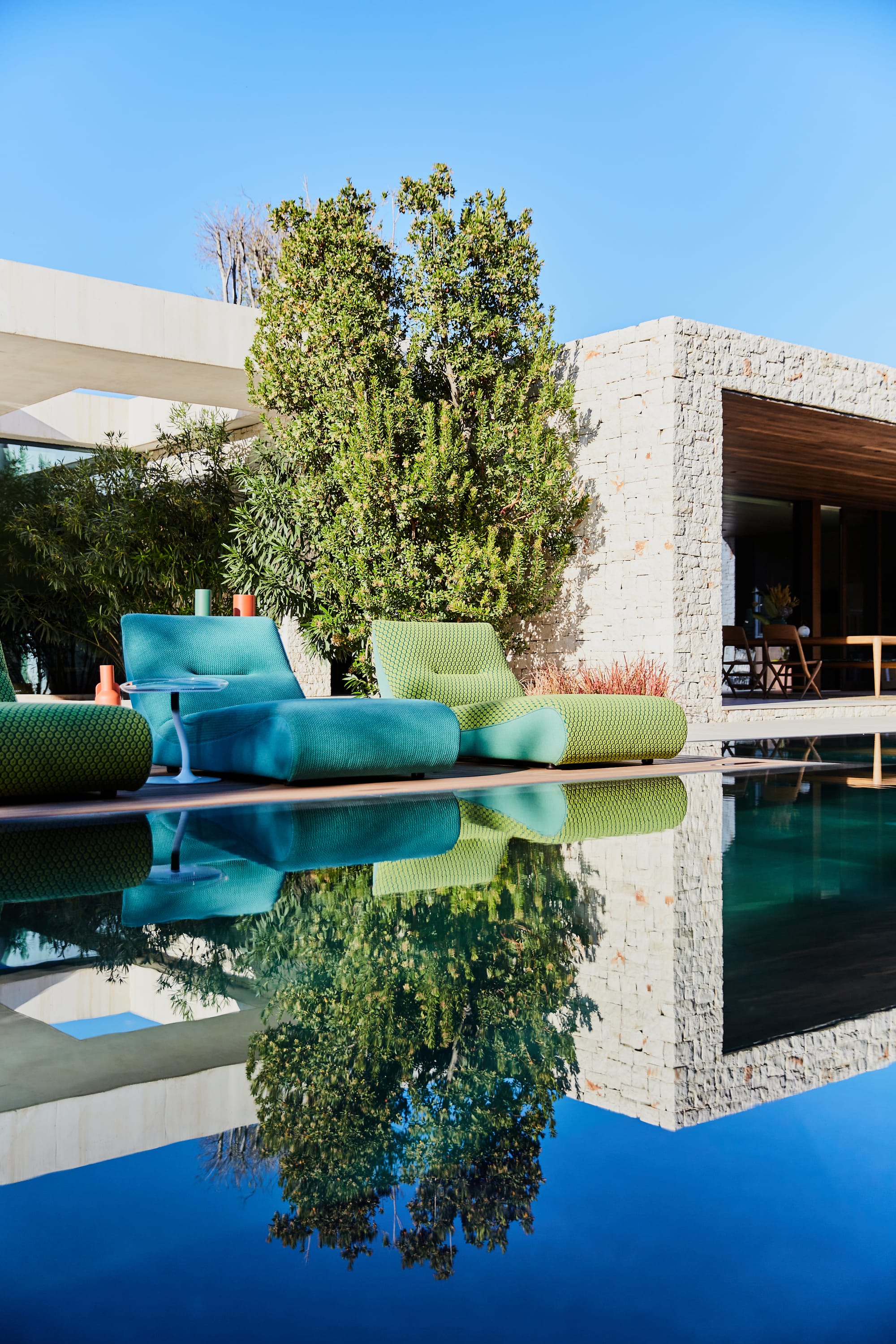 Outdoor Collection by Roche Bobois. Turquoise outdoor foam sun beds next to modern house and pool.