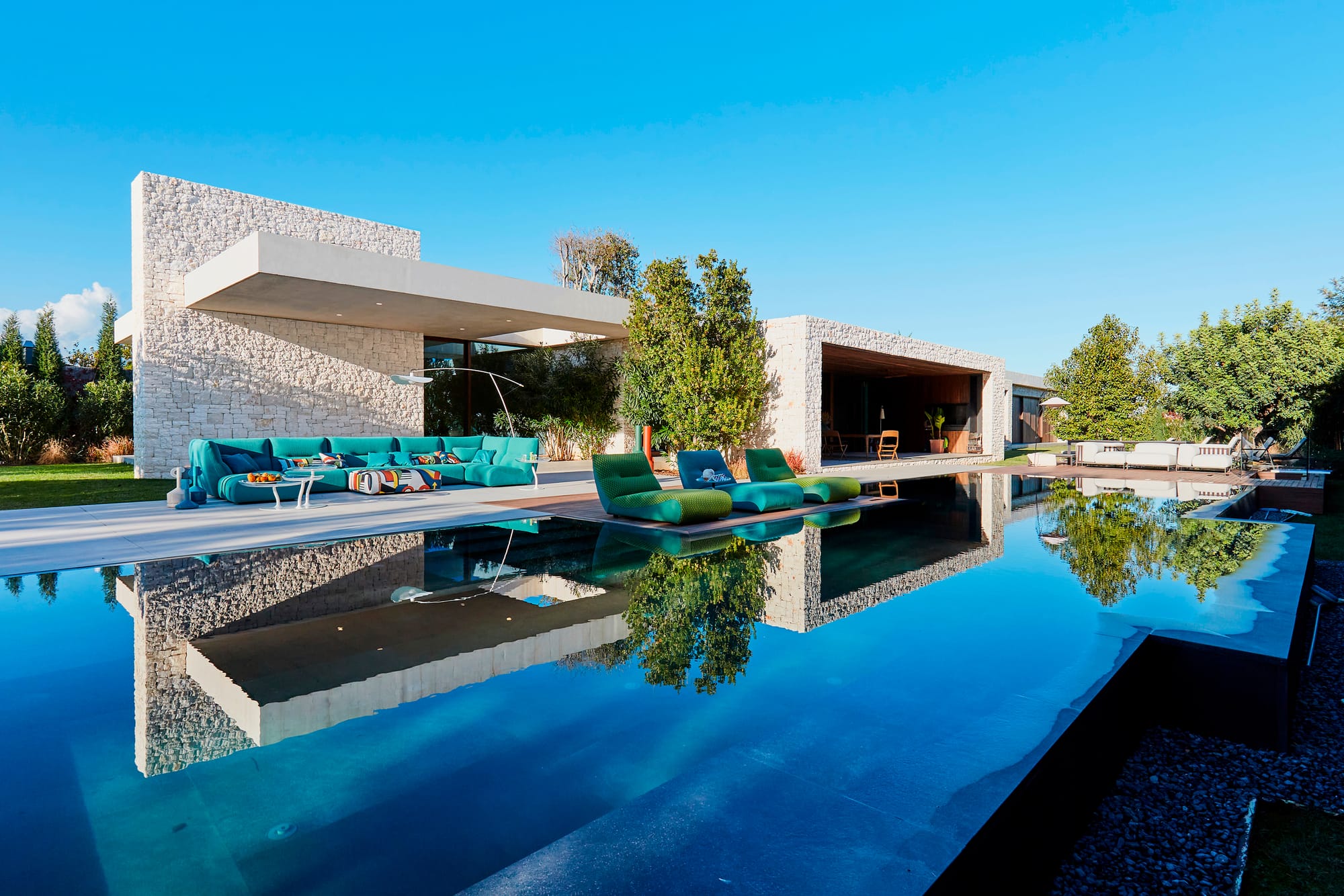 Outdoor Collection by Roche Bobois. Turquoise outdoor sofa and foam sun beds next to modern house and pool.