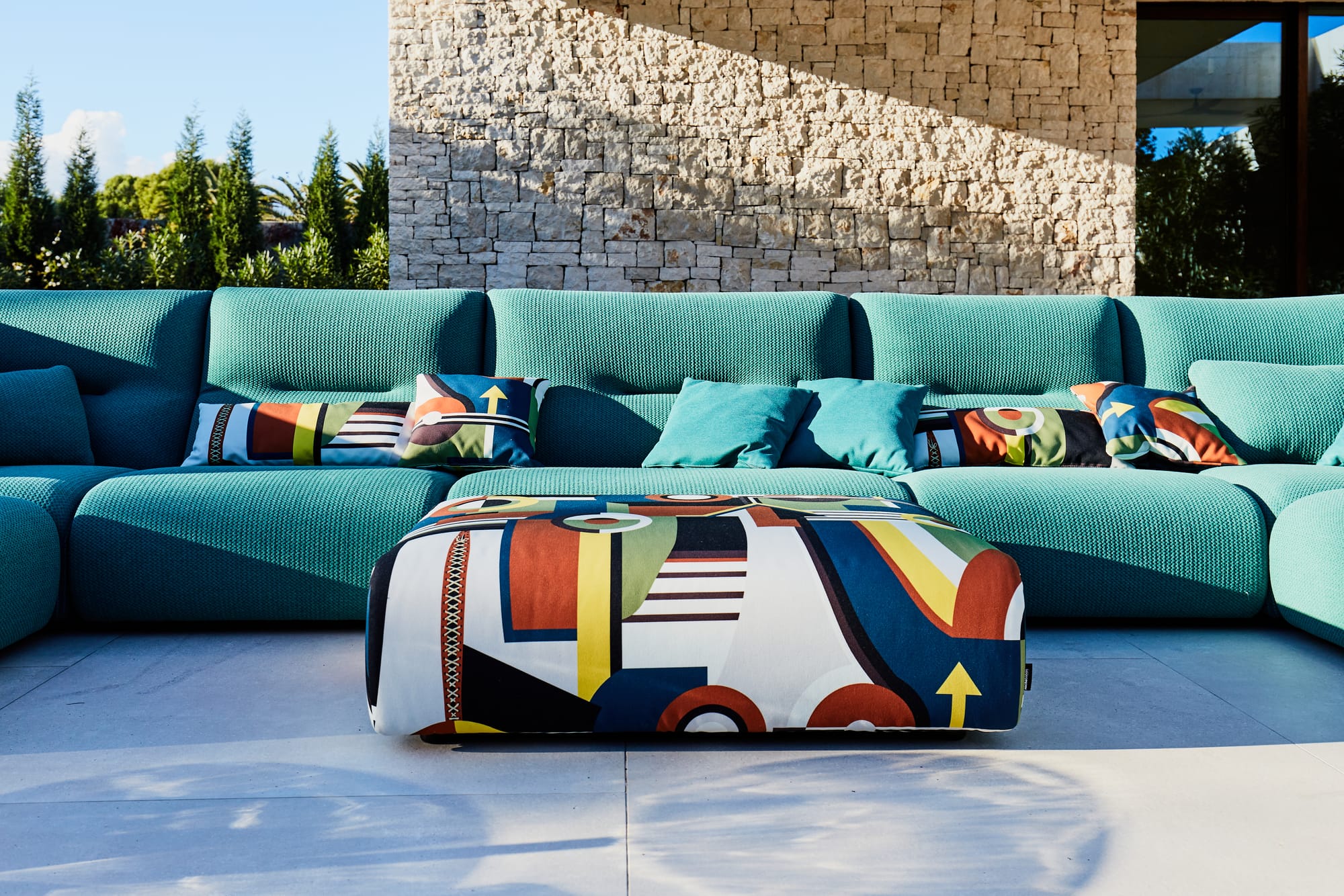 Outdoor Collection by Roche Bobois. Turquoise outdoor sofa next to modern house.