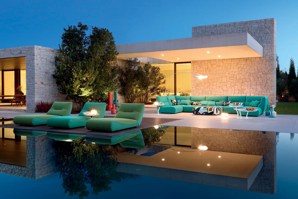 Outdoor Collection by Roche Bobois. Turquoise outdoor sofa and foam sun beds next to modern house and pool.