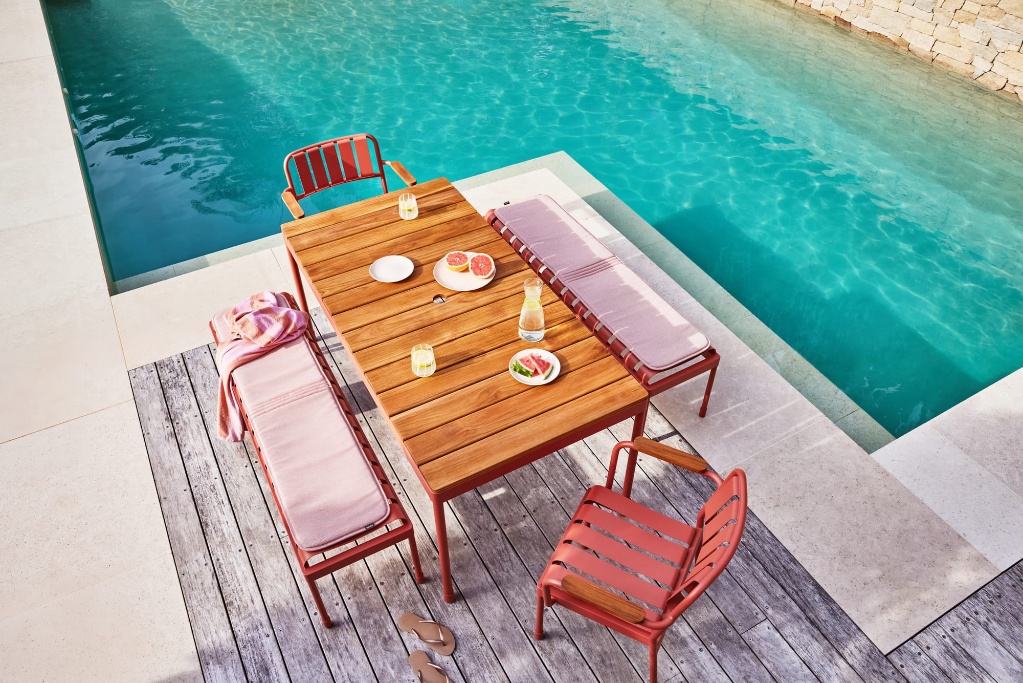 Torakina Outdoor by Koala Living. Pool area with outdoor Dining Set featuring 3 seater benches and armchairs with local oak and coral red steel frame, roundly shaped.