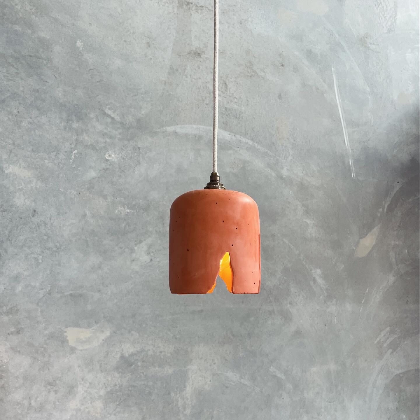 Wattle Pendant in Terracotta. Image copyright of Crete Studio. Terracotta concrete pendant light with crack in front of grey concrete wall.