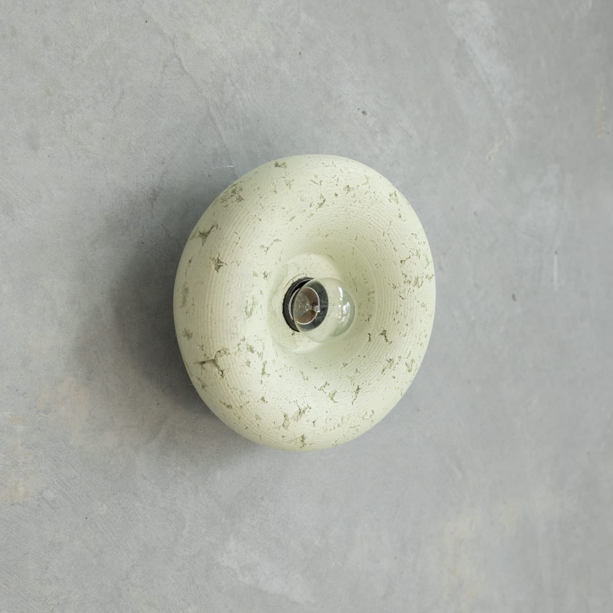 Haze Wall Sconce in Moss. Image copyright of Crete Studio. Light sage green puffed round wall sconce with raw texture on concrete wall. 