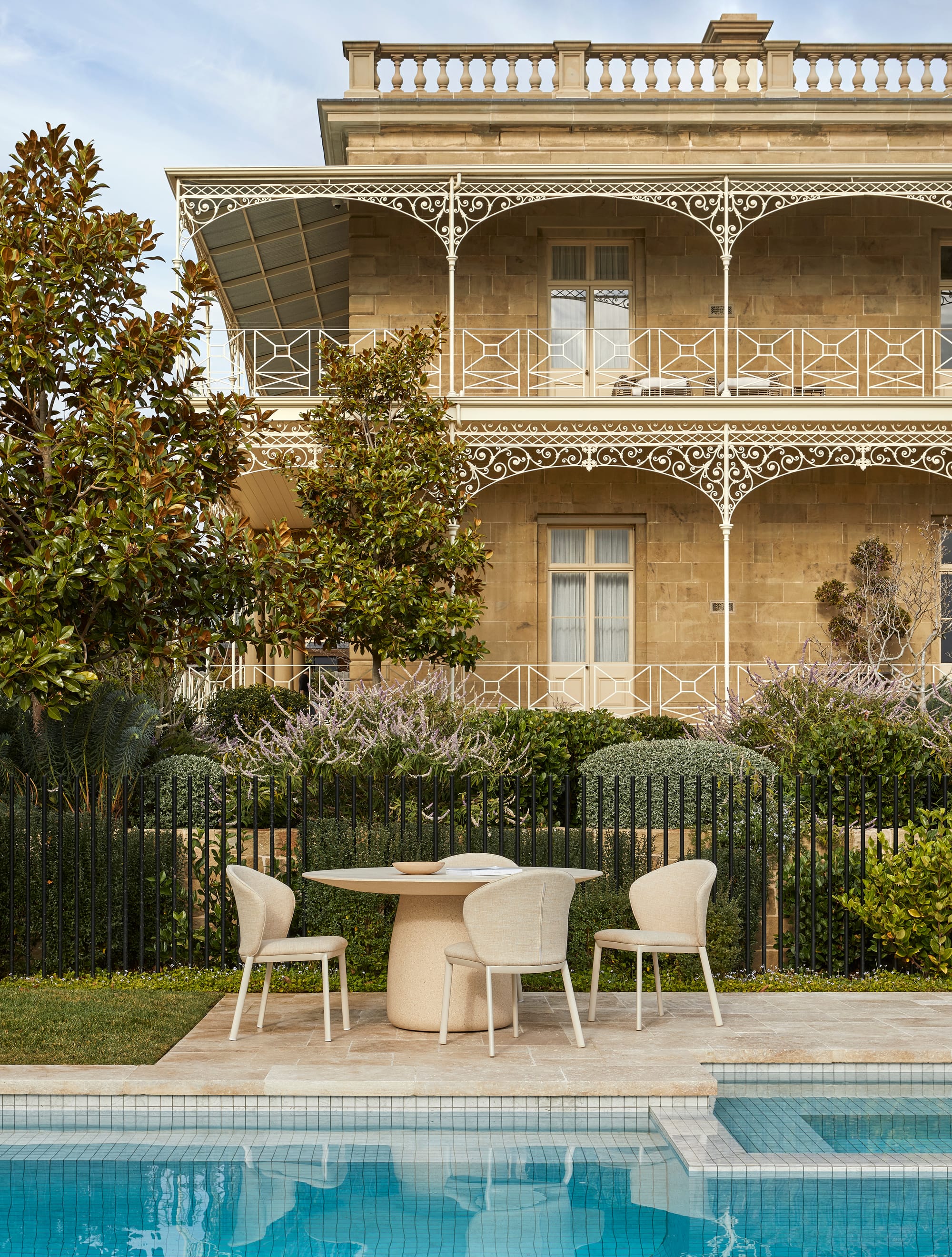 Melba Outdoor Dining Table & Dining Chairs by GlobeWest. Dining set at pool in front of Mediterranean house with garden.