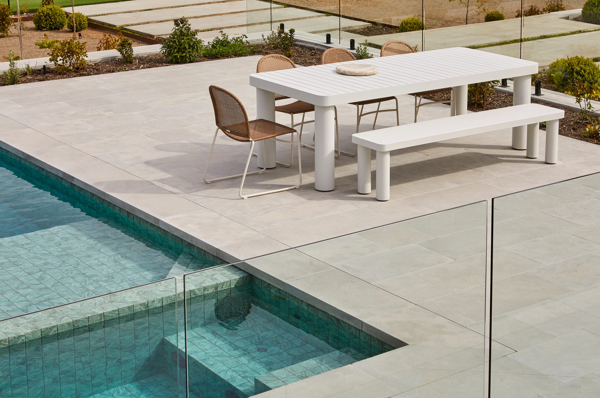 Frankie Outdoor Dining Table & Bench Seat by GlobeWest. Outdoor dining set featuring white modern table and rattan chairs at pool.