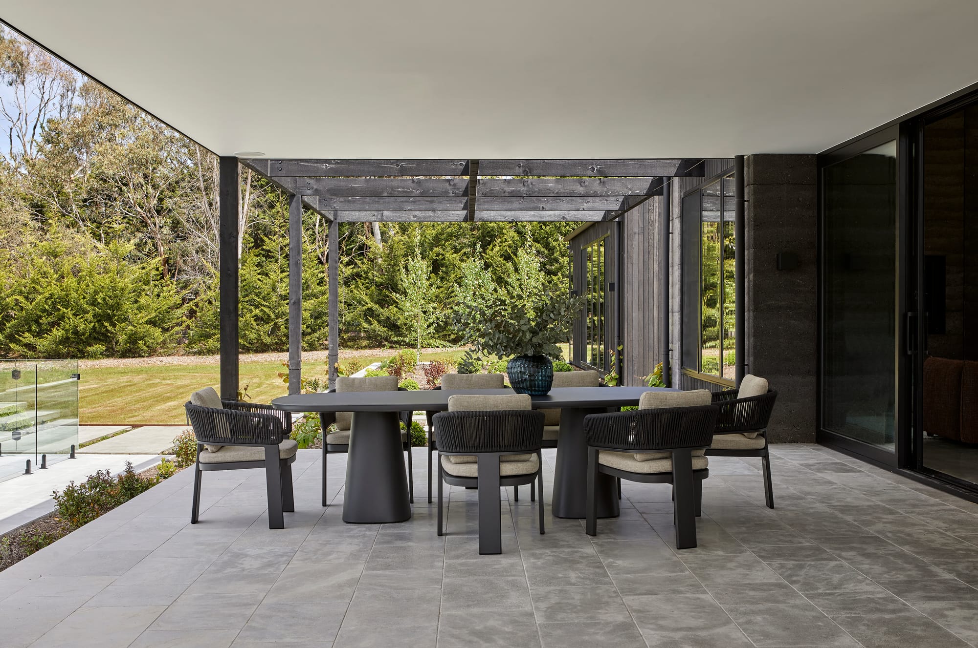 Valencia Dining Table & Valencia Rope Dining Chairs by GlobeWest. Loggia with dining table and chairs featuring black powder coated aluminum frame and beige cushions.