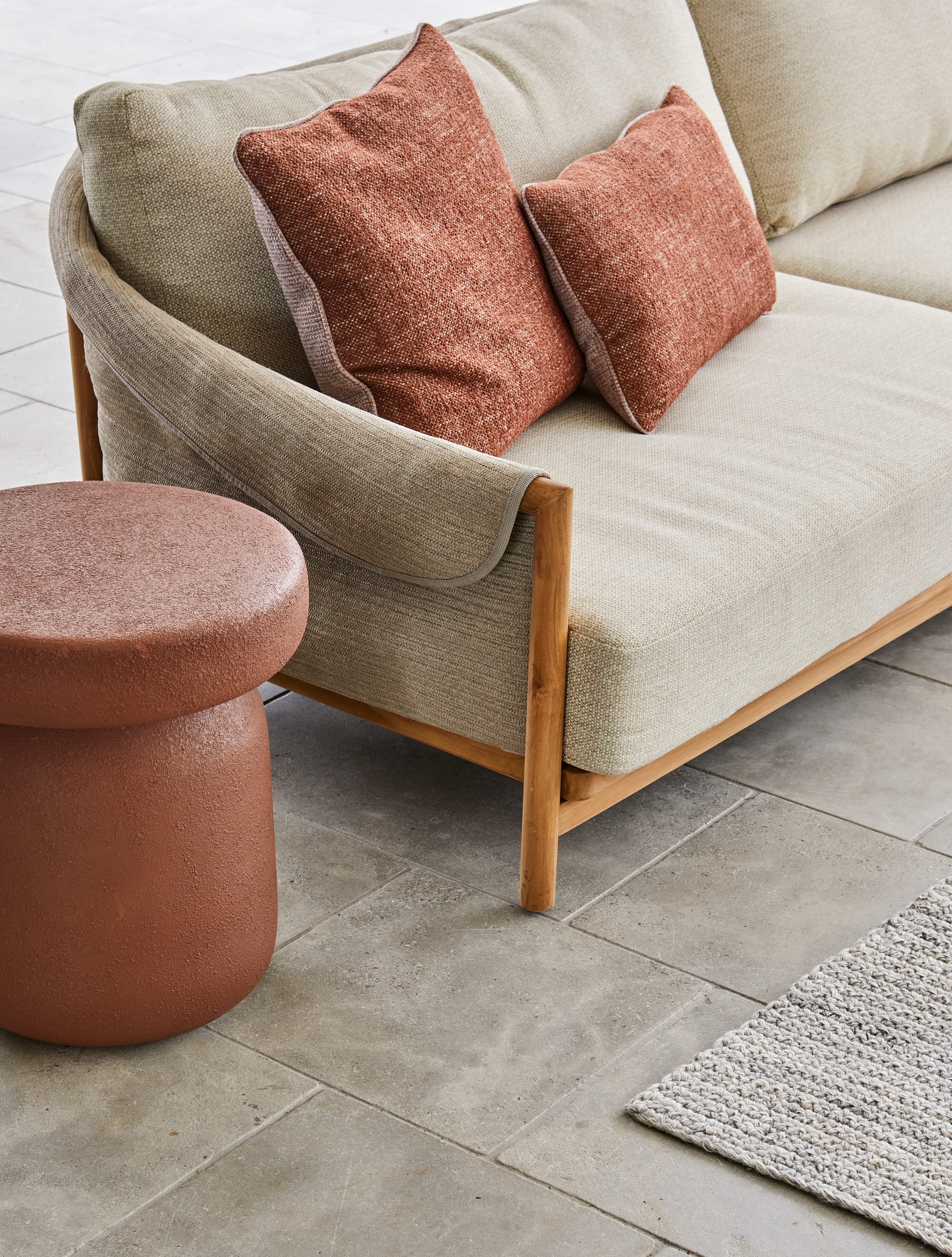 Grao 3 Seater Sofa & Granada Button Side Table by GlobeWest. Detail of outdoor sofa featuring beige fabric and clay colored cushions and clay coloured coffee table.