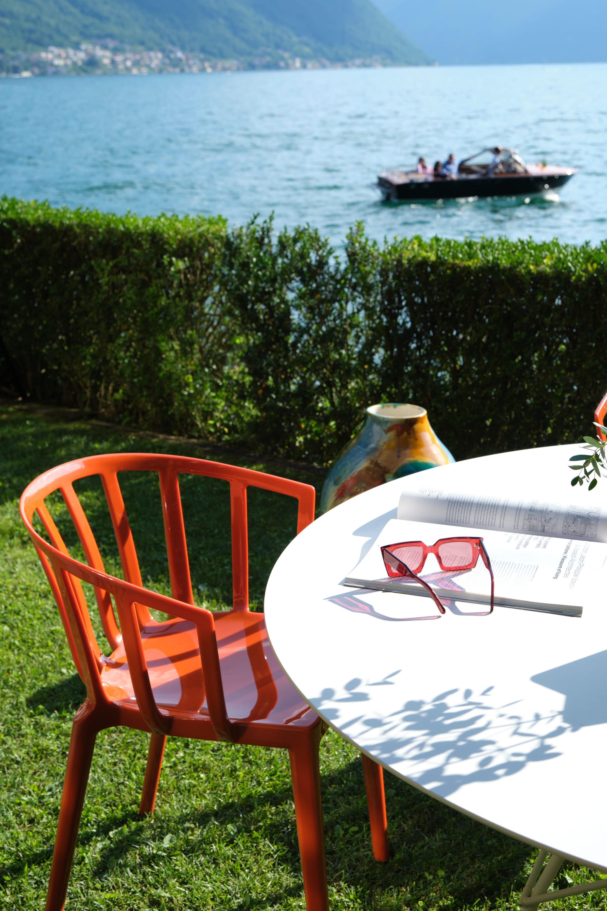 Outdoor Collection Venice Chair by KartellPerth. Red polyurethane outdoor chair and white round outdoor dining table next to lake and Mediterranean landscape.