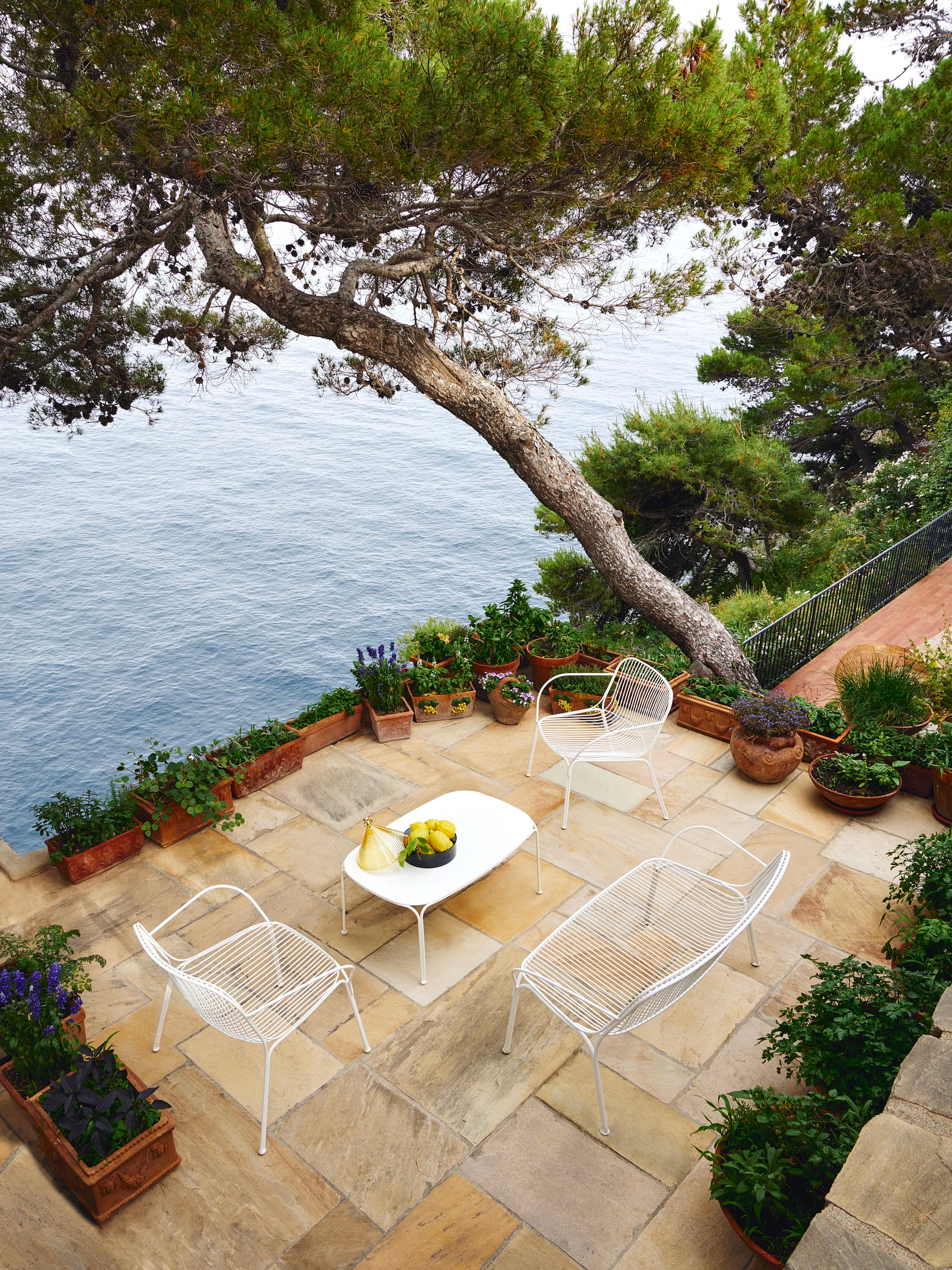 Outdoor Collection Hiray by KartellPerth. White powder coated steel dining set featuring 2 seater and armchairs on Mediterranean terrace next to lake.