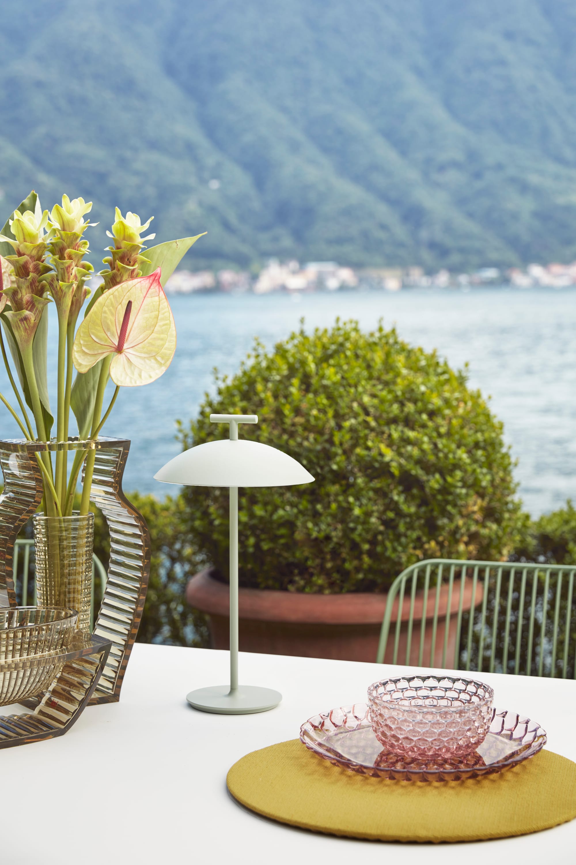 Outdoor Collection Jellies by KartellPerth. Detail of polyurethane plating and vases on table next to lake and vegetated mountains. 