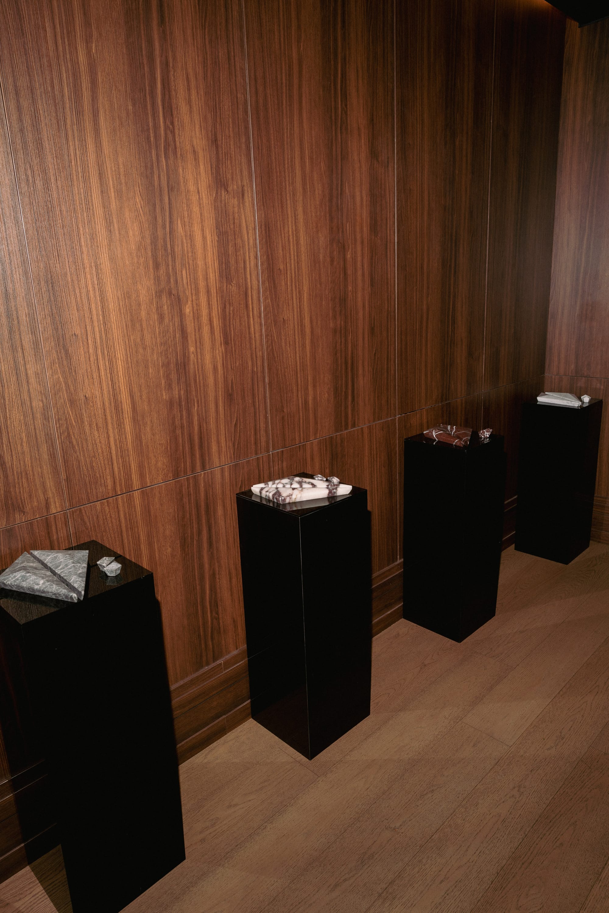 PRISM collection by Lo & Co. Black, grey, white and red marble triangular handles and edgy knobs displayed on black cubes in front of wooden wall.