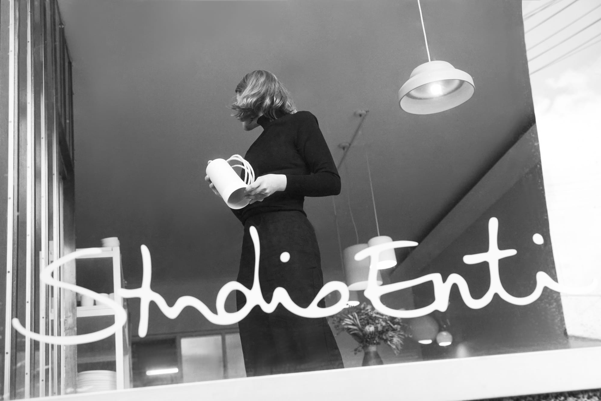 Naomi standing in the Studio Enti front window with Studio Enti branding on the glass