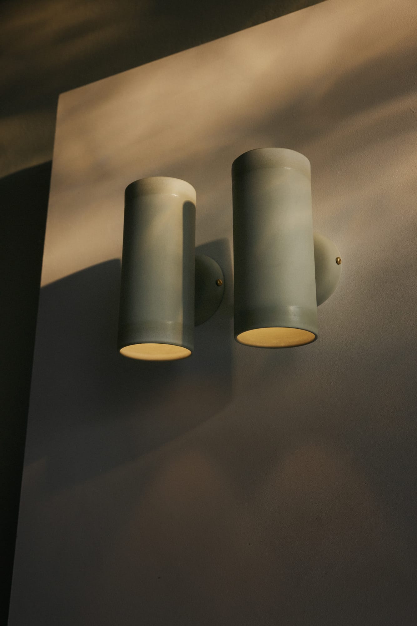 Porcelain Eos Wall Lights by Studio Enti on a brown wall with a warm yellow glow.