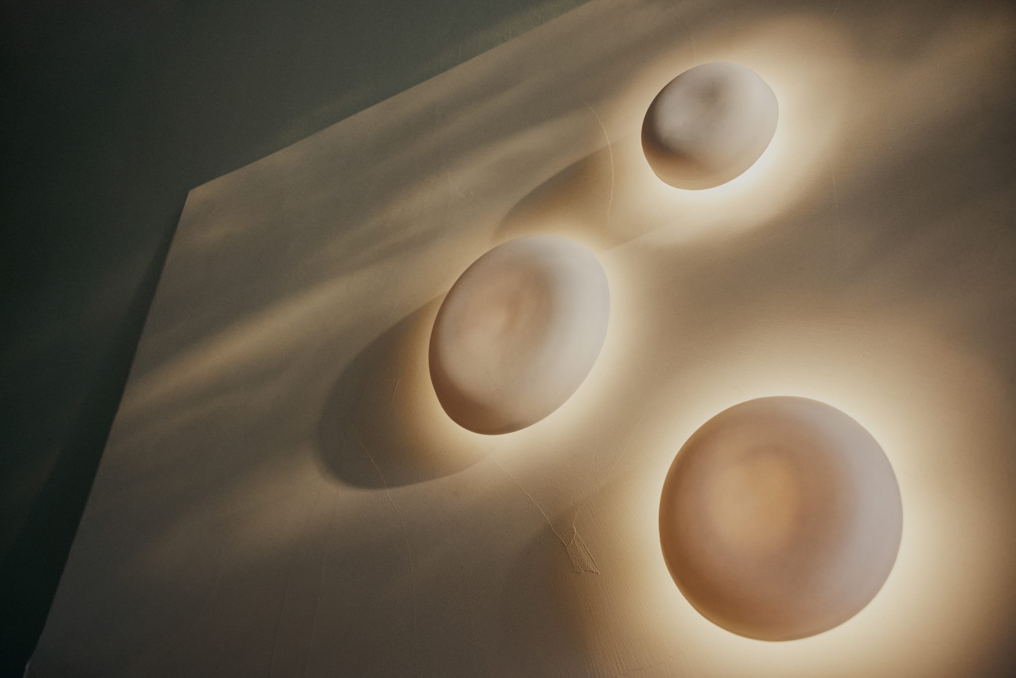 Eclipse Sconces by Studio Enti on a wall with light shining from them.