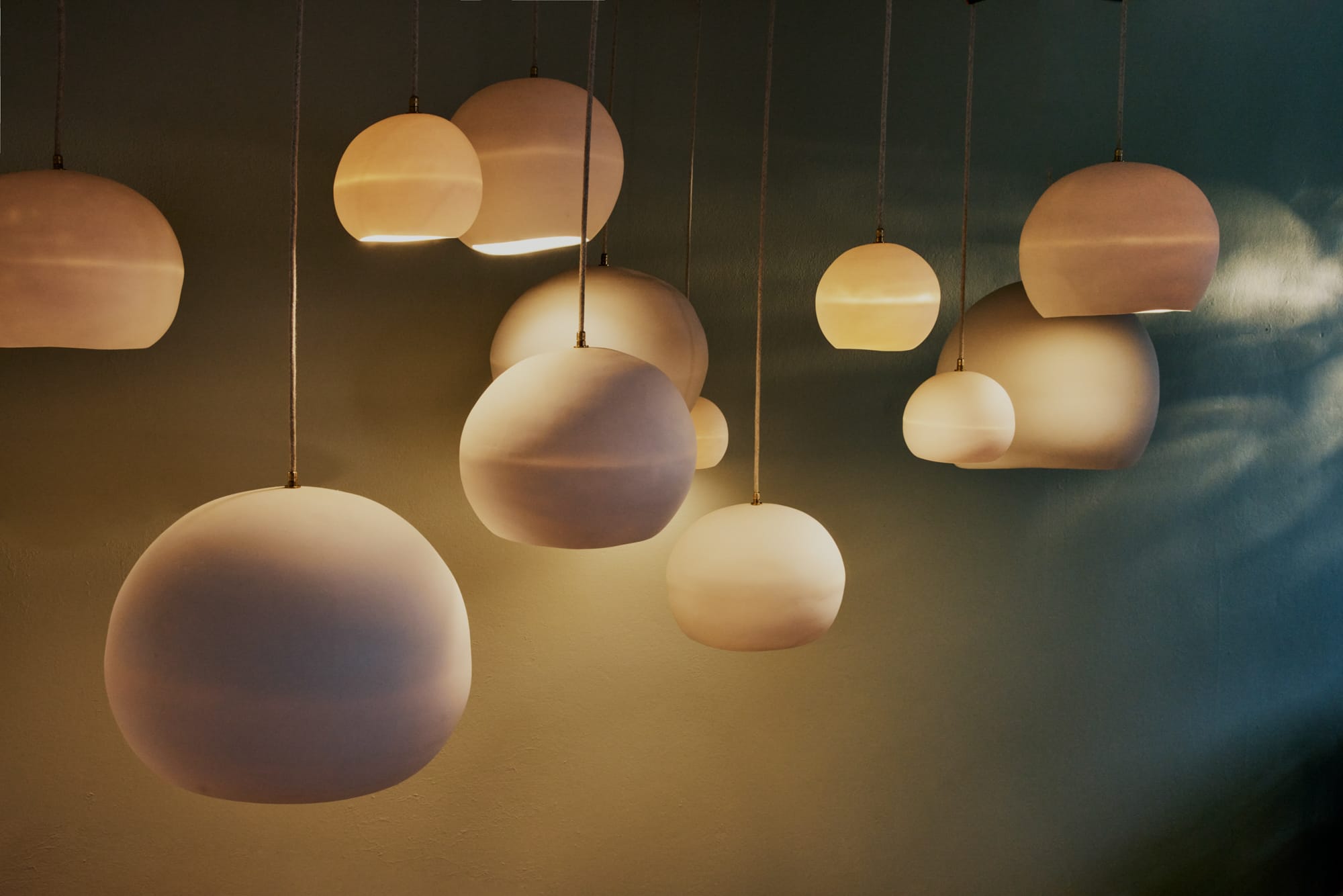 Orb Pendant Lights by Studio Enti hanging in various sizes and with warm yellow glow