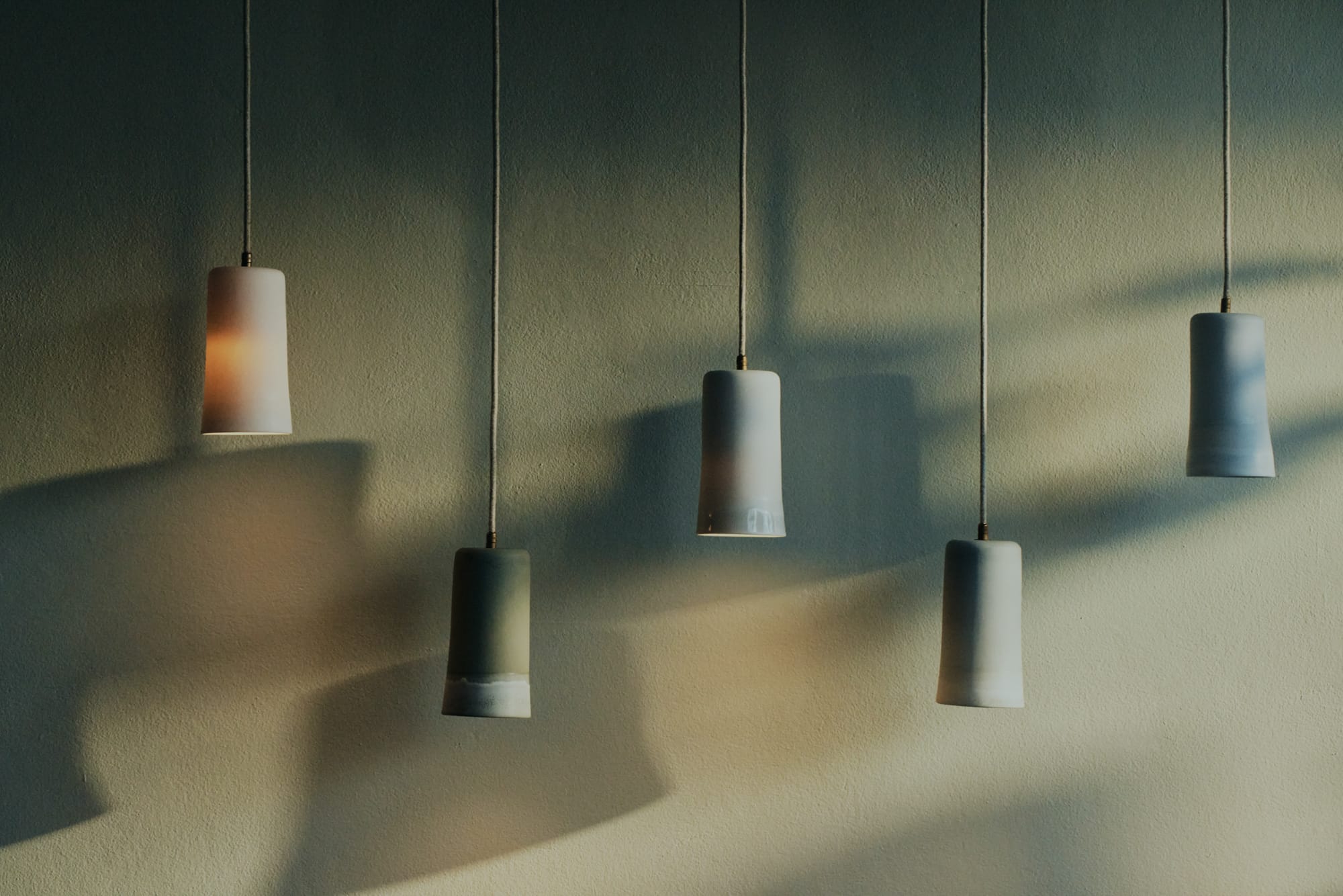 A collection of The Dusked Pendants by Studio Enti hanging in a variety of colours against a rendered wall.