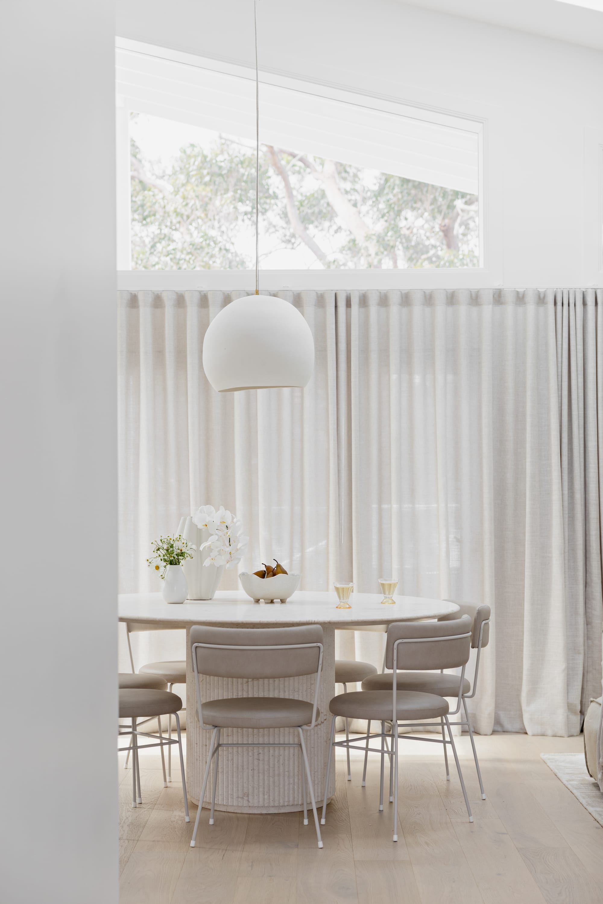 Orb Pendant Light by Studio Enti hanging over a white dining table with a white curtain in the background.