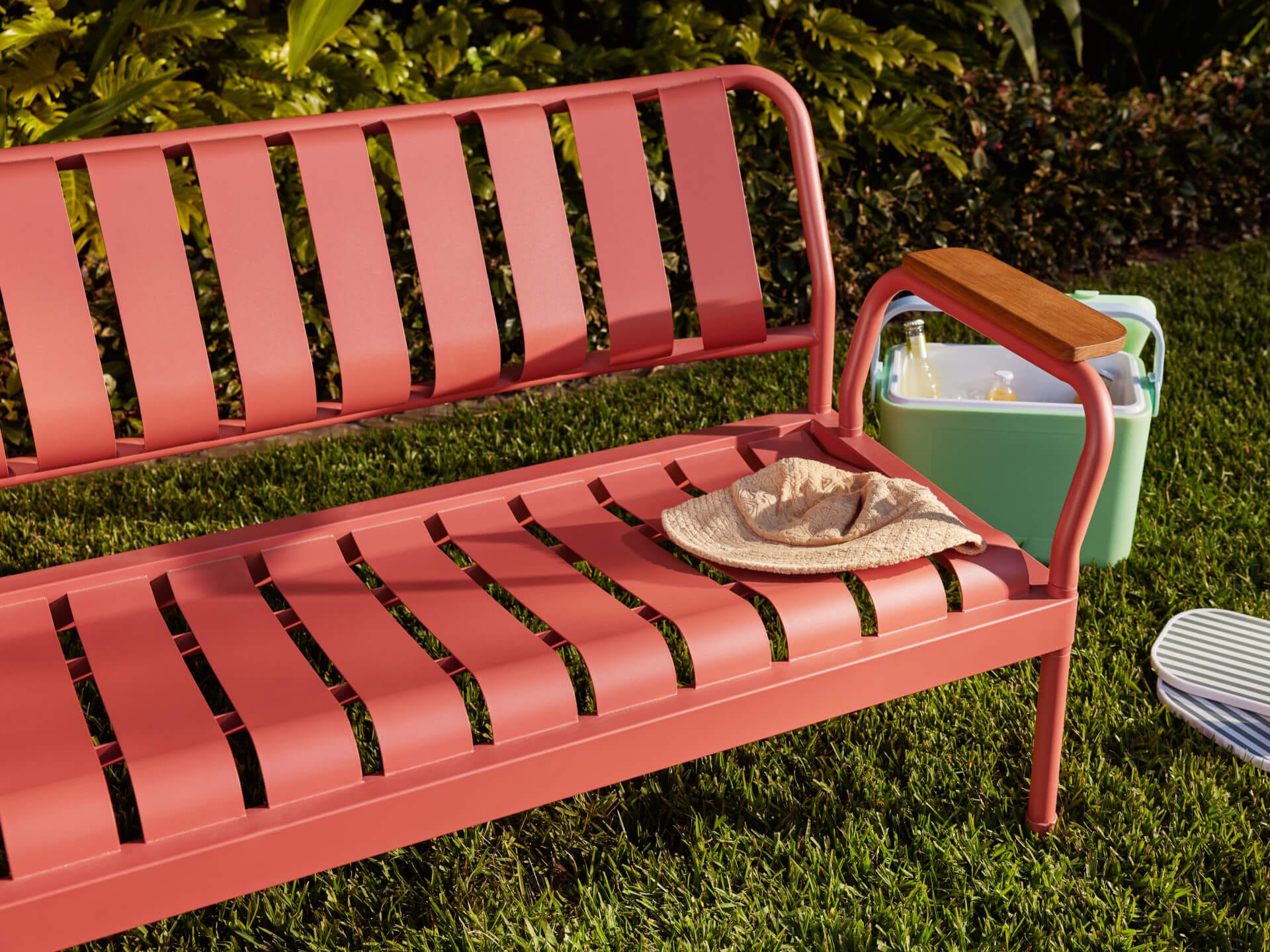 Torakina Outdoor Lounge Set by Koala in Outback Rose. Pink metal bench seat on grass, with green esky and garden in background.