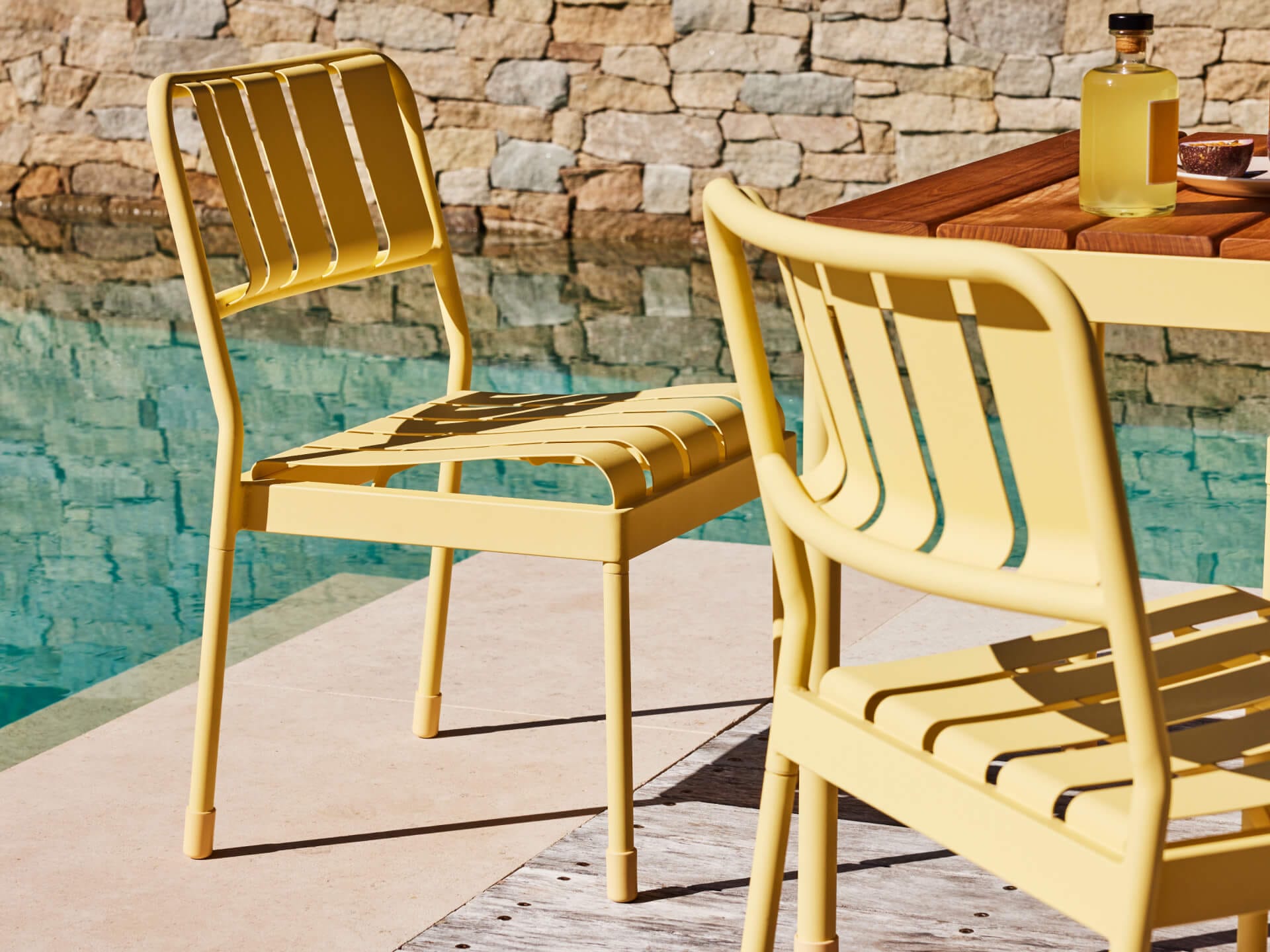 Torakina Outdoor Dining Seating by Koala in Beach Walk. Close up shot of two yellow metal chairs in front of timber dining table and pool. 