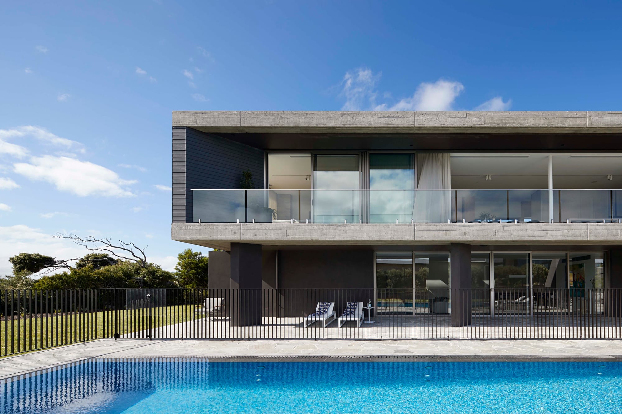 Wildcoast Road by Rachcoff Vella Architecture. Photography by Shannon McGrath. Double storey contemporary concrete building with glass balcony and long pool. 