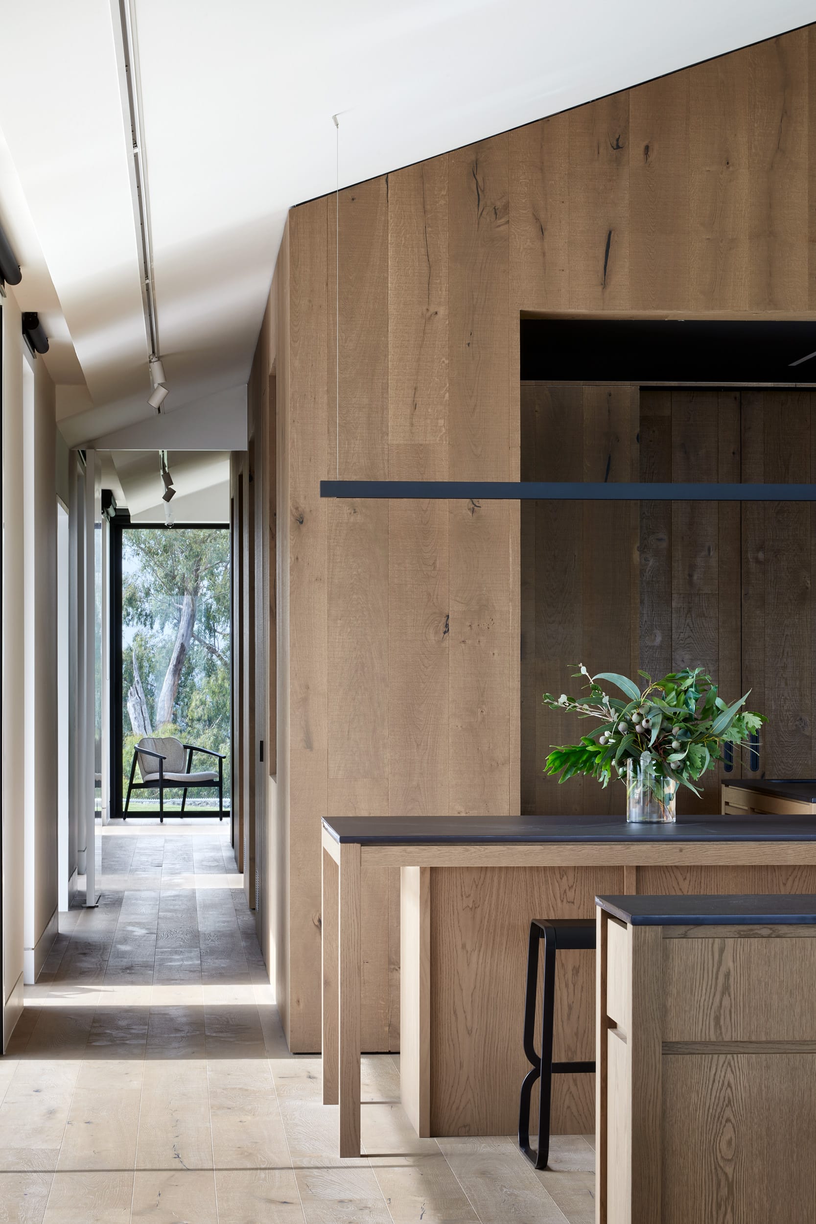 Gruyere Farmhouse by Rachcoff Vella Architecture. Photography by Tatjana Plitt. Timber kitchen and flooring leading down hallway with floor-to-ceiling windows. 