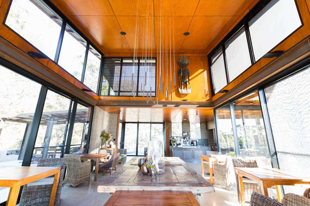 Spicers Sangoma by Barbara Tarnawski Architects. Low angle of dining space with high timber ceilings, glass windows and doors and hanging pendant lights.