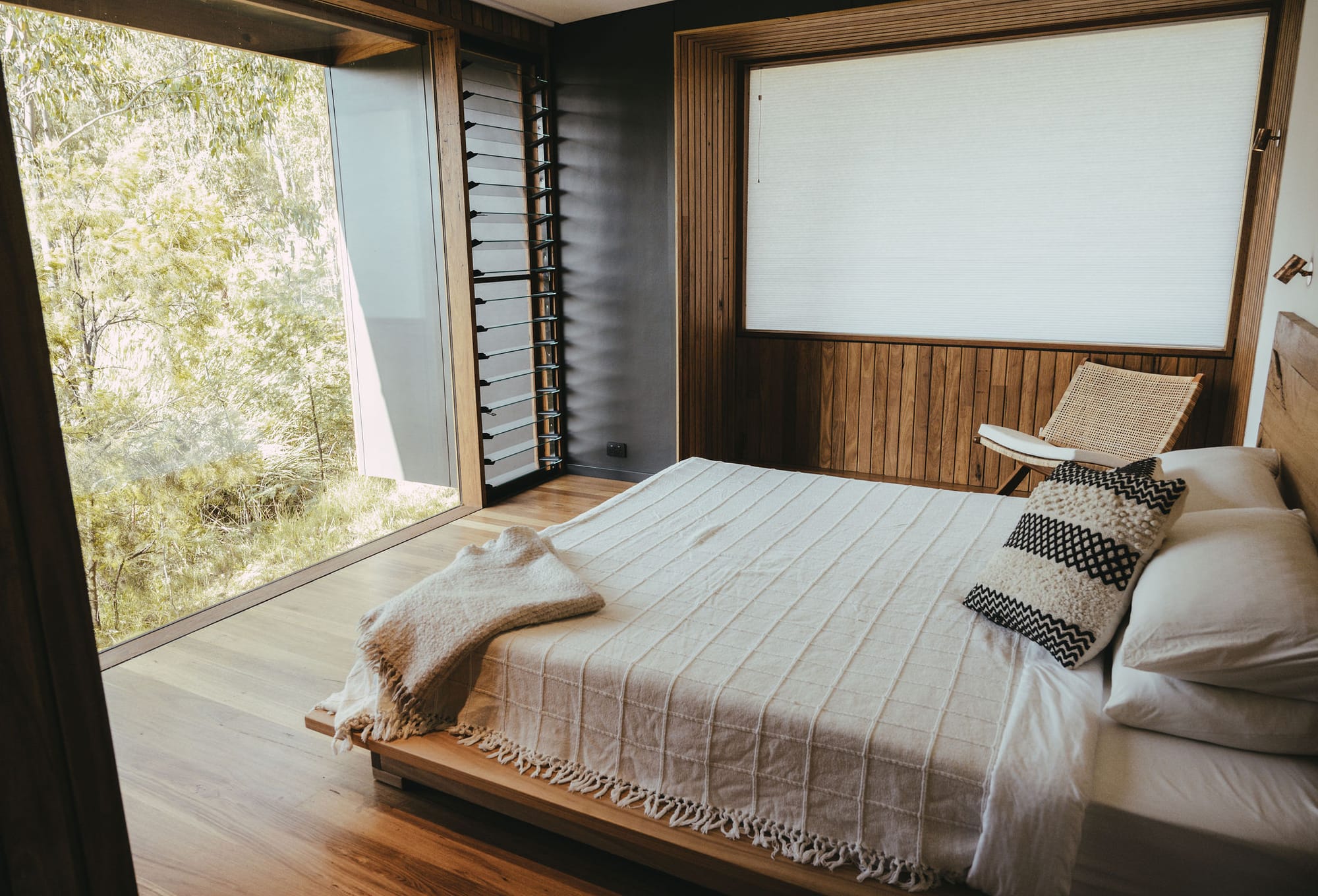 The Summer House at Little Valley Farm. Photography by Milou Hofman Photography. Bedroom with floor to ceiling window overlooking the bushland, with white bedspread and pillows on bed.