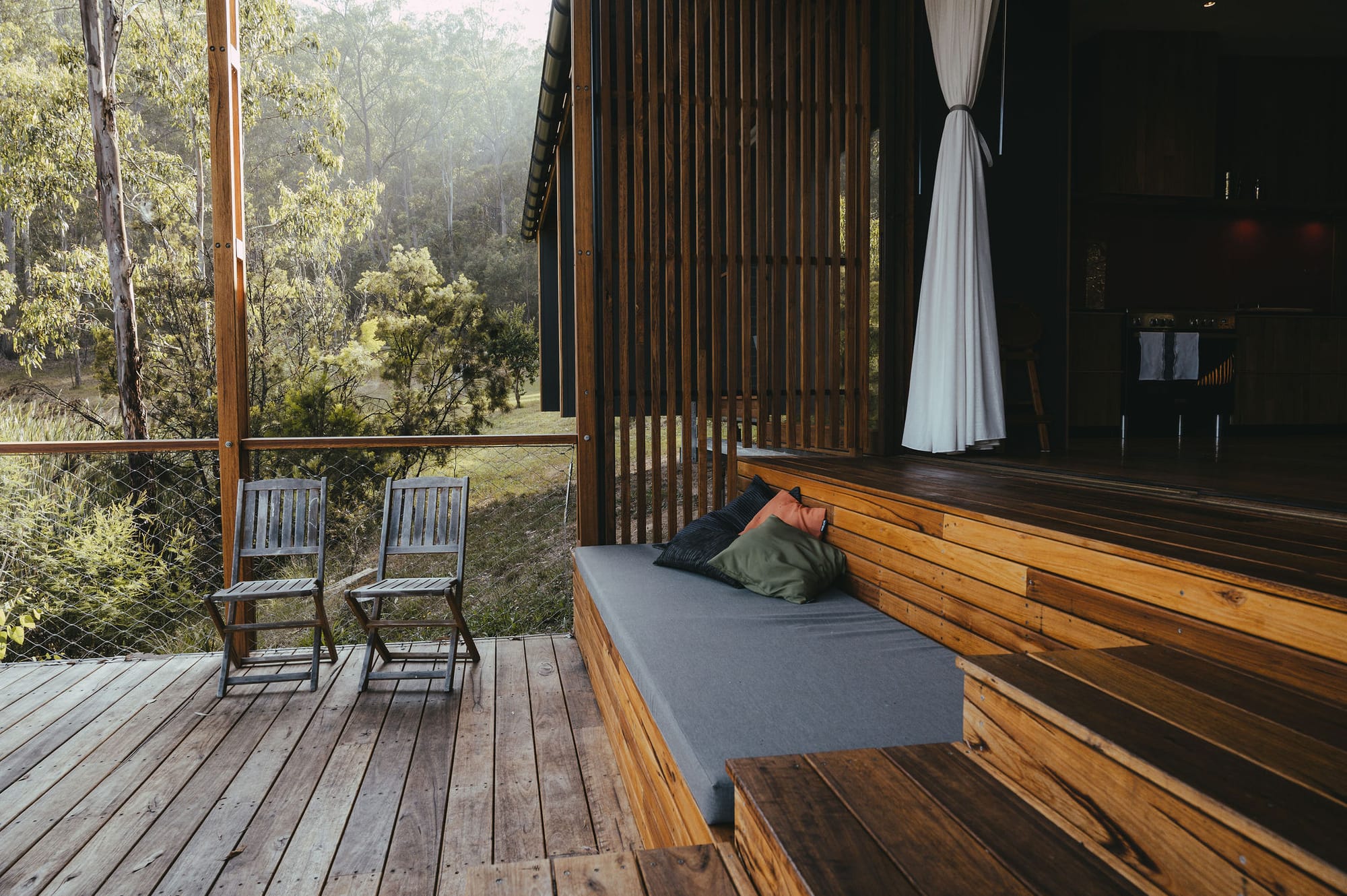 The Summer House at Little Valley Farm. Photography by Milou Hofman Photography. Outdoor seating area with bench seating integrated into timber steps and decking, with fencing overlooking native bushland.