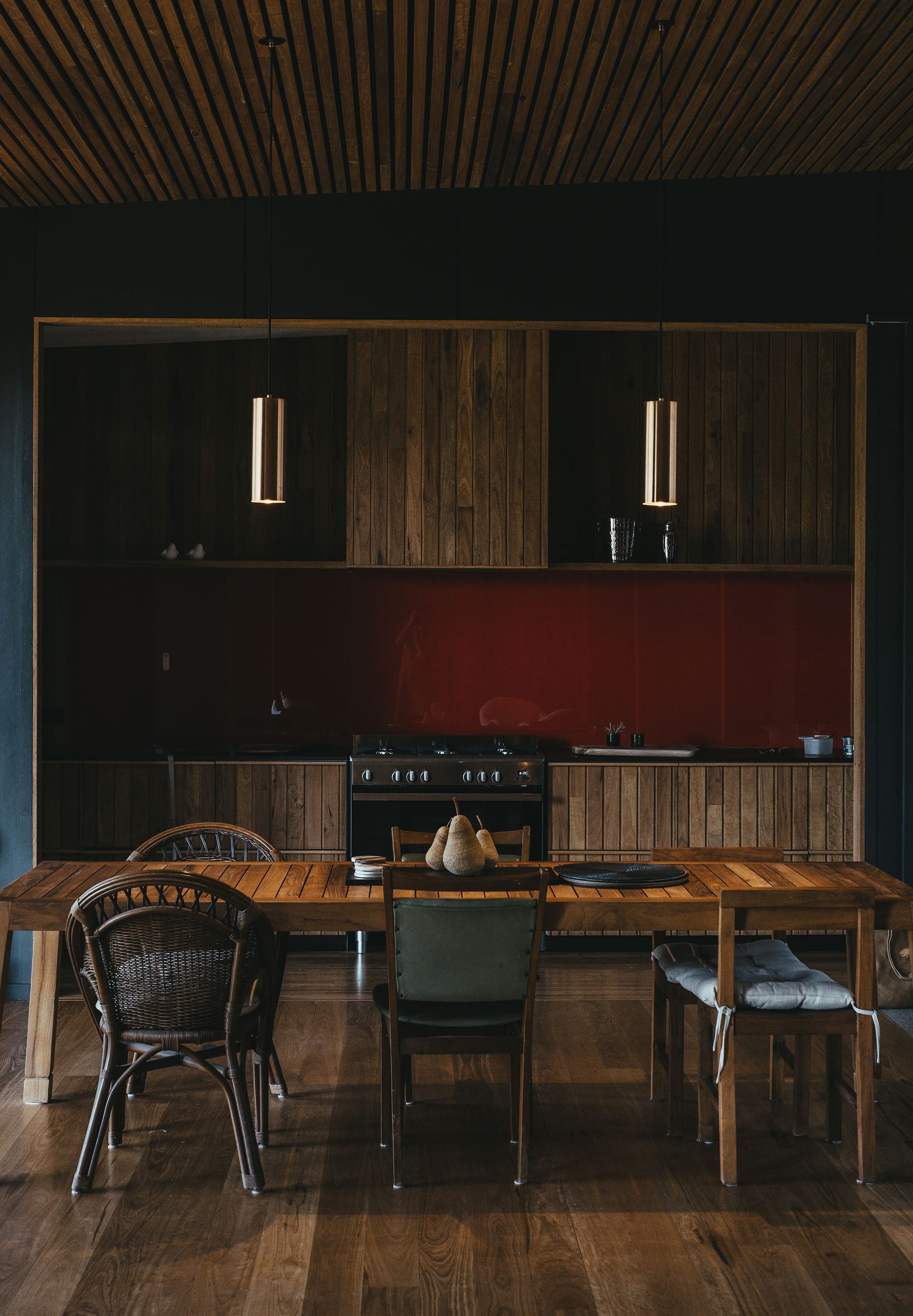 The Summer House at Little Valley Farm. Photography by Milou Hofman Photography. Open plan dining and kitchen space with timber floors and joinery, red splashback and mismatched dining chairs.