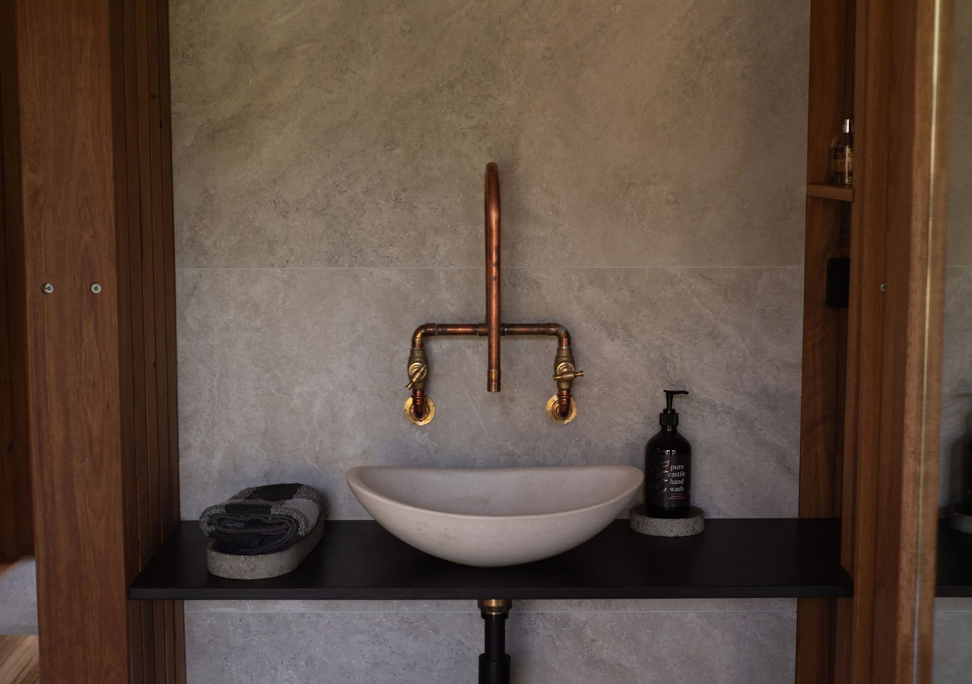 The Summer House at Little Valley Farm. Photography by Milou Hofman Photography. Bathroom with freestanding porcelain sink with tiled splashback, timber storage and brass fixtures. 