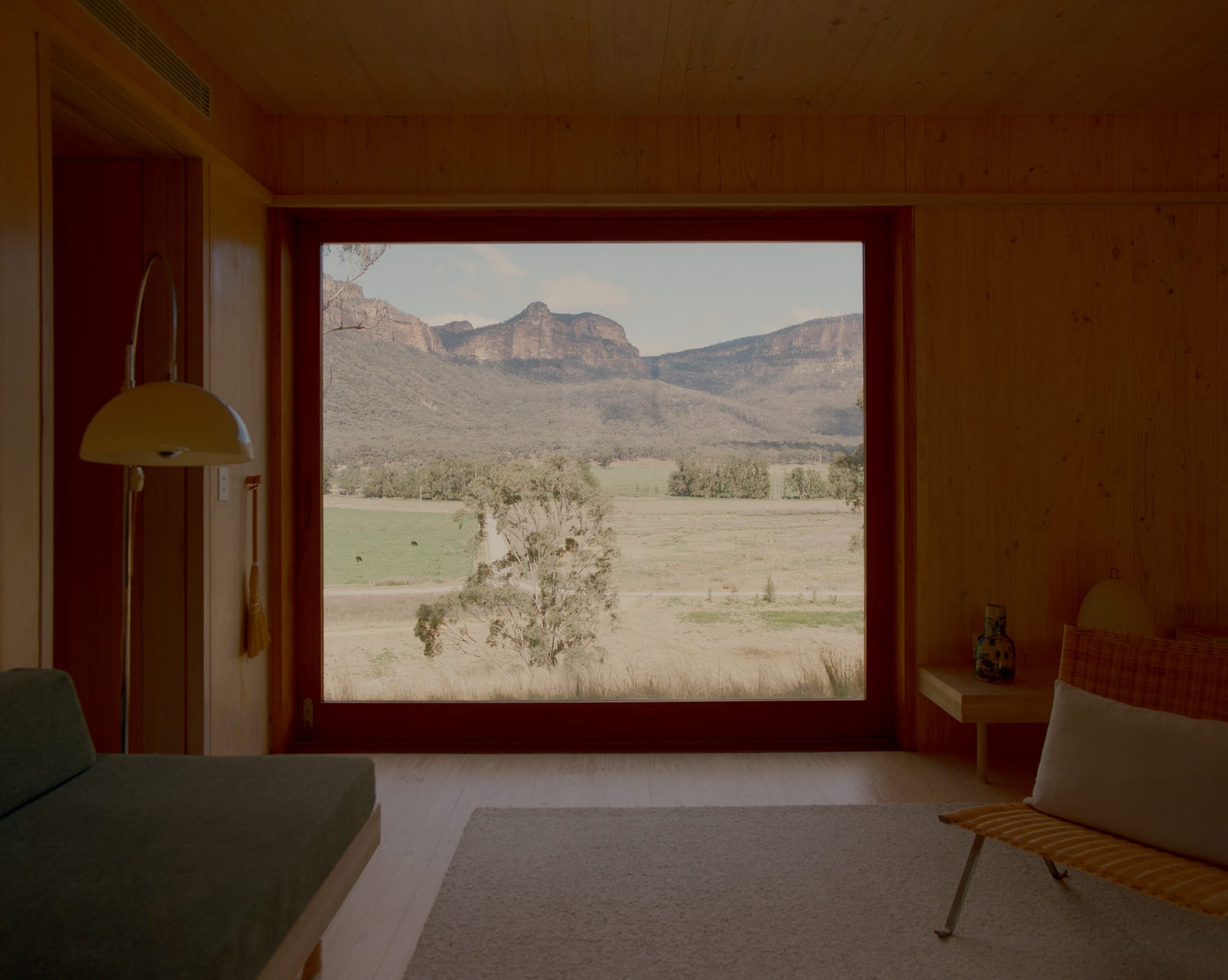 Practice Ground. Photography by Saskia Wilson. Timber and glass sliding door framing rustic open plain bushland outside of timber clad interior. 