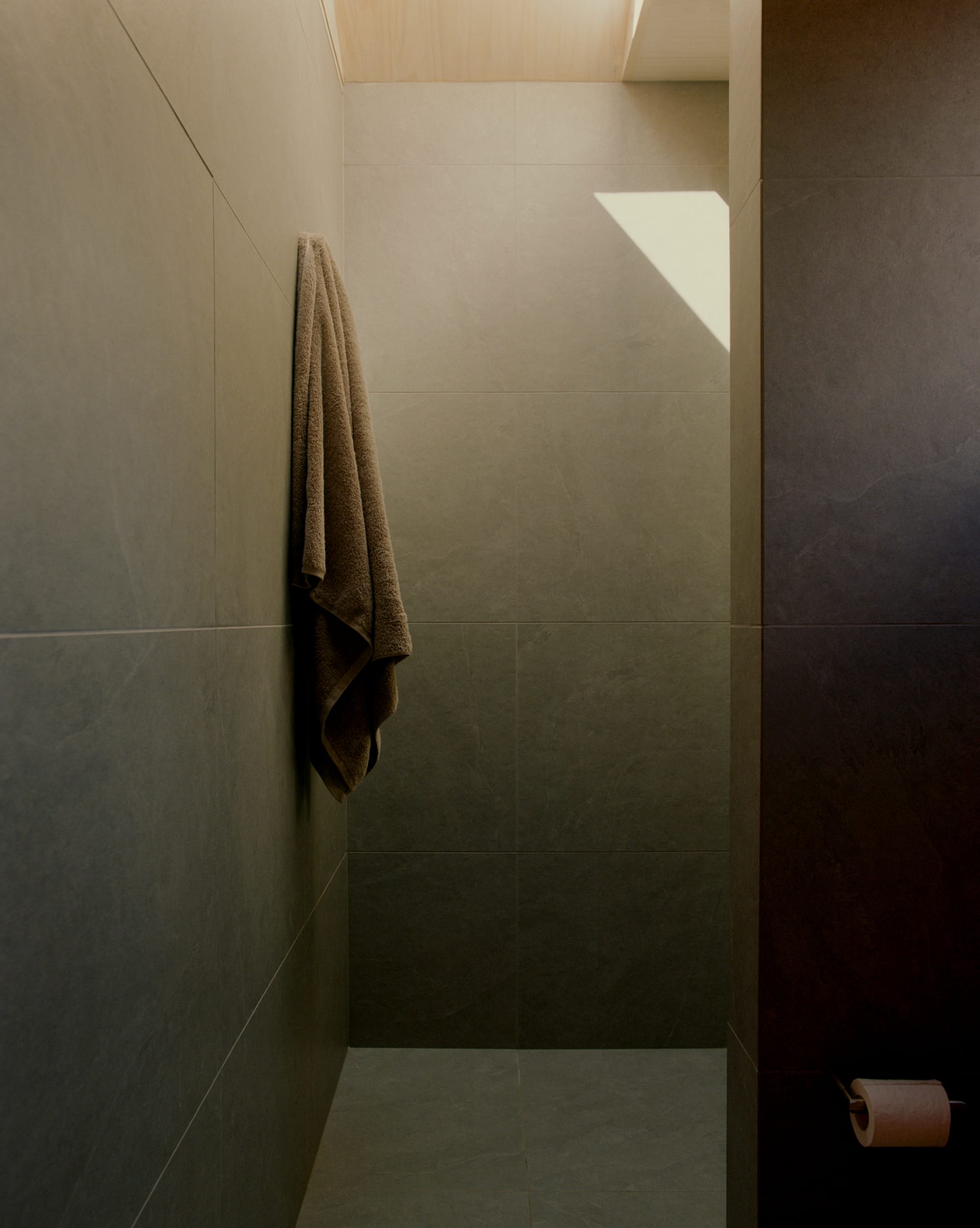 Practice Ground. Photography by Saskia Wilson. Dark slate tiled shower with skylight and single towel hanging on left wall. 